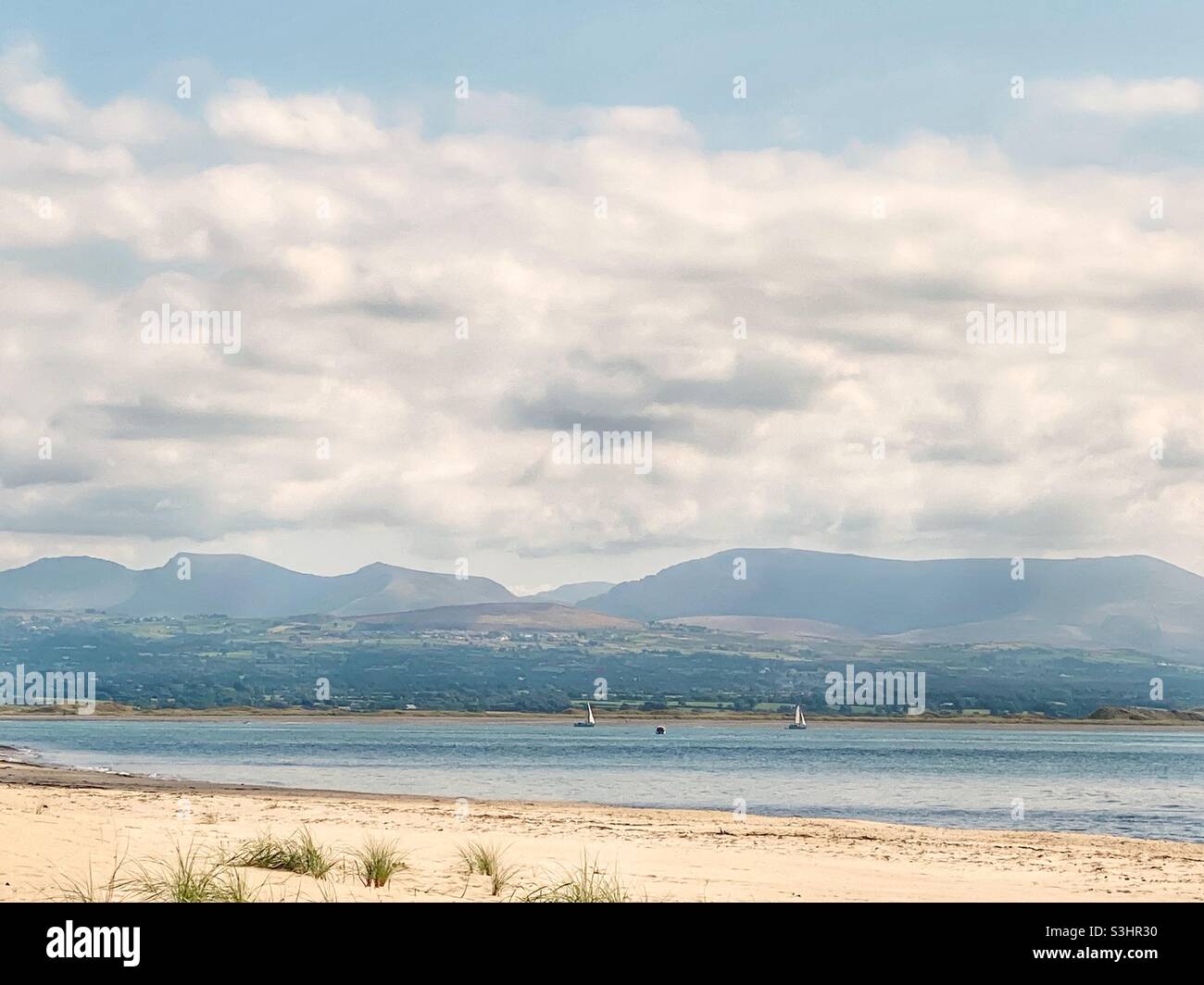 Vista di Snowdonia attraverso lo stretto di Menai dalla spiaggia a Newborough Warren, Anglesey, Galles del Nord, Regno Unito - Immagine stock catturata con smartphone