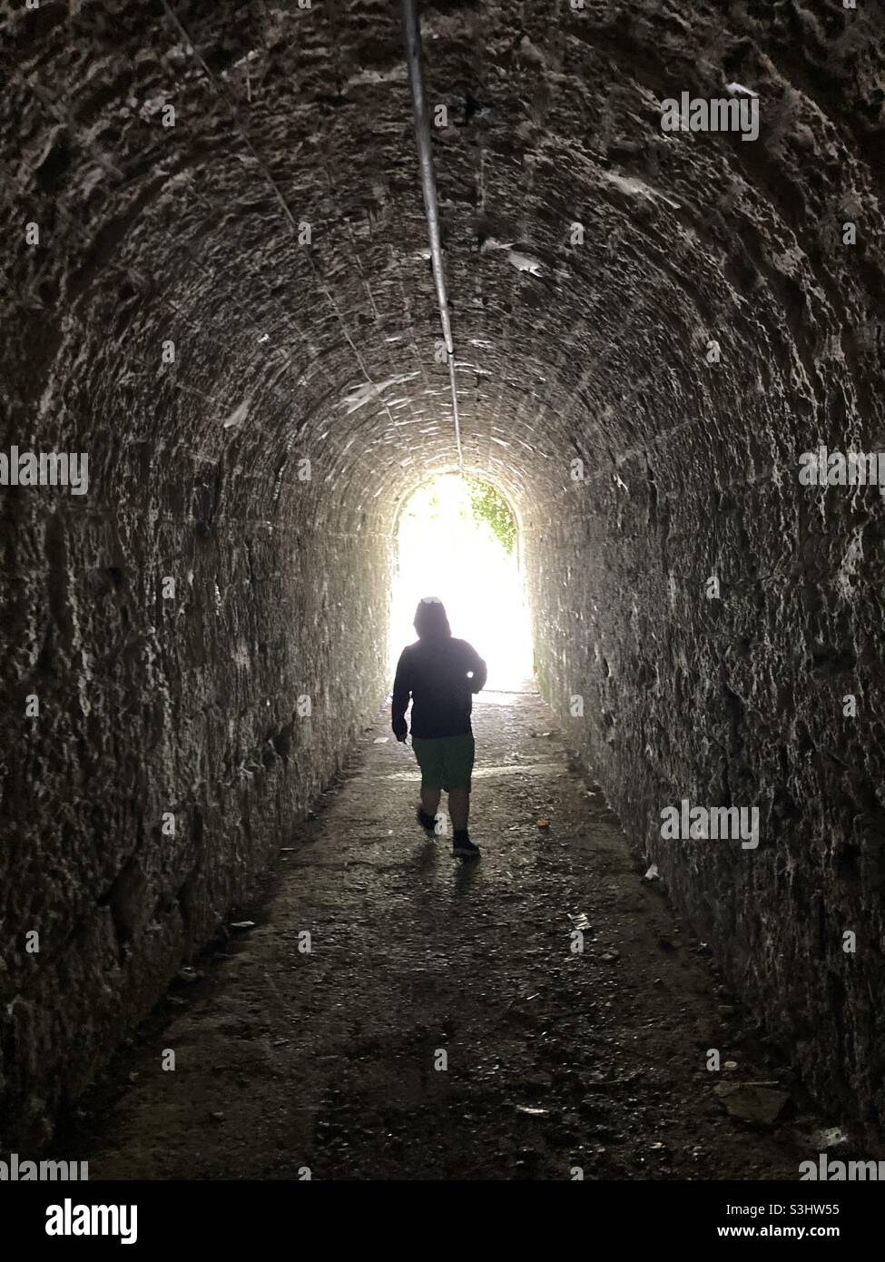 Anonimo silhouette di un uomo a piedi attraverso un sottopassaggio buio che simboleggia la luce alla fine del tunnel - Immagine stock catturata con smartphone