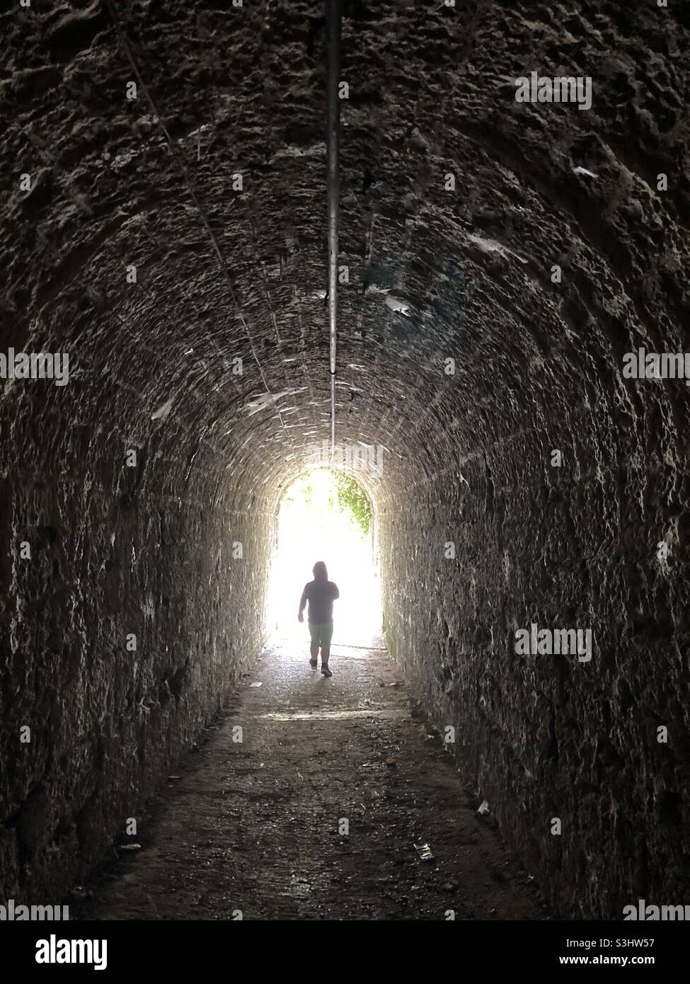 Anonimo silhouette di un uomo a piedi attraverso un sottopassaggio buio che simboleggia la luce alla fine del tunnel - Immagine stock catturata con smartphone