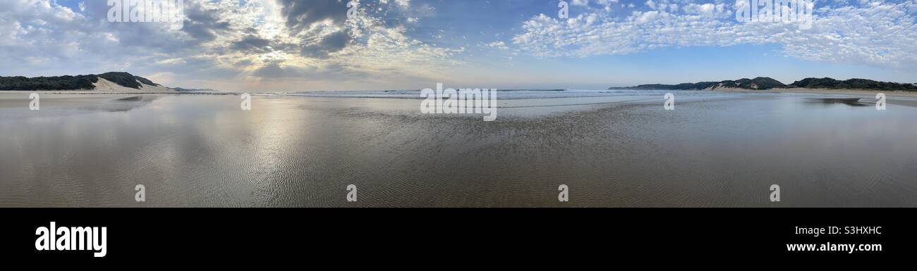 Spiaggia panoramica durante un sorgere del sole nuvoloso Foto Stock