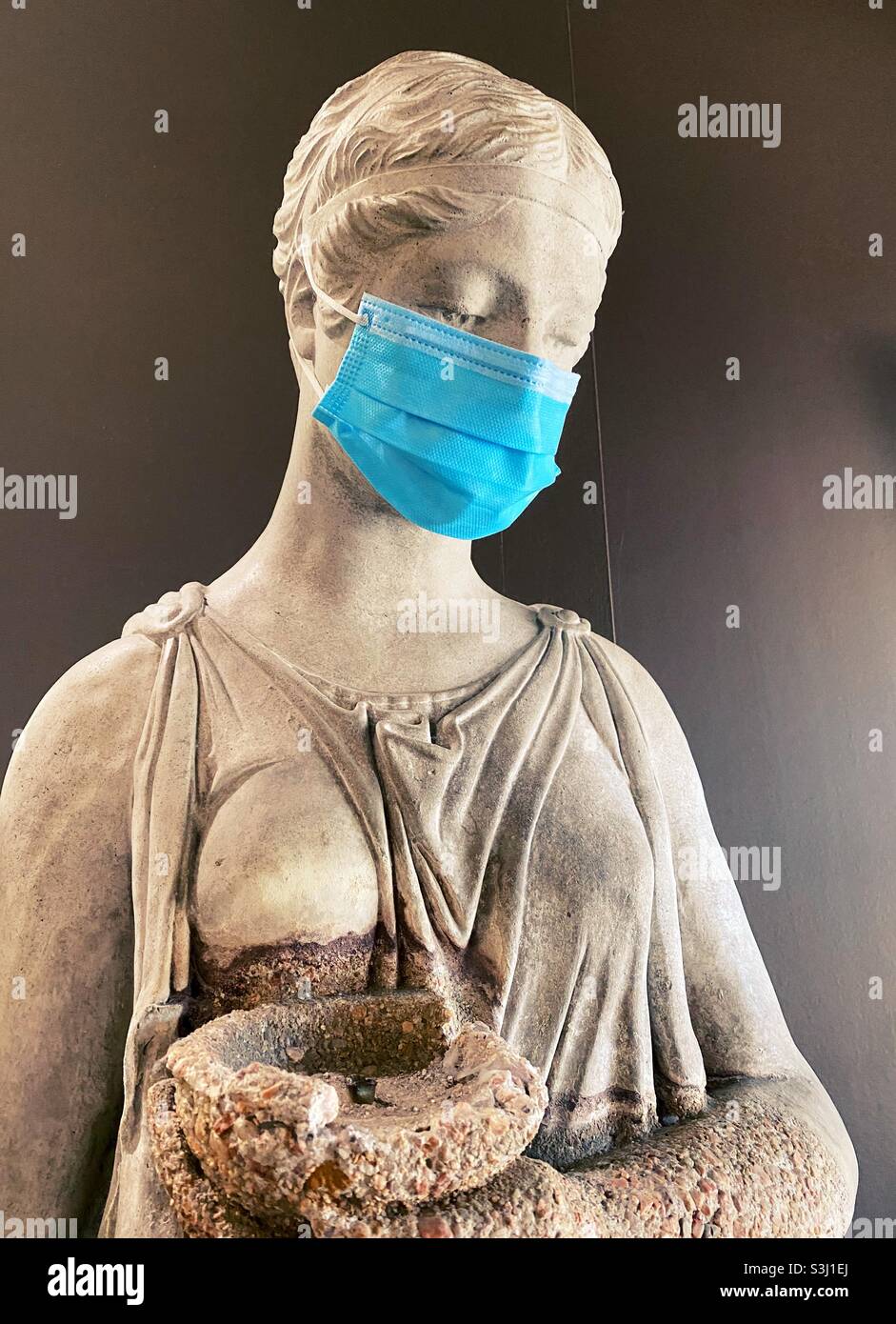 Una statua in stile antico di una donna, che indossa una moderna maschera chirurgica. Foto Stock