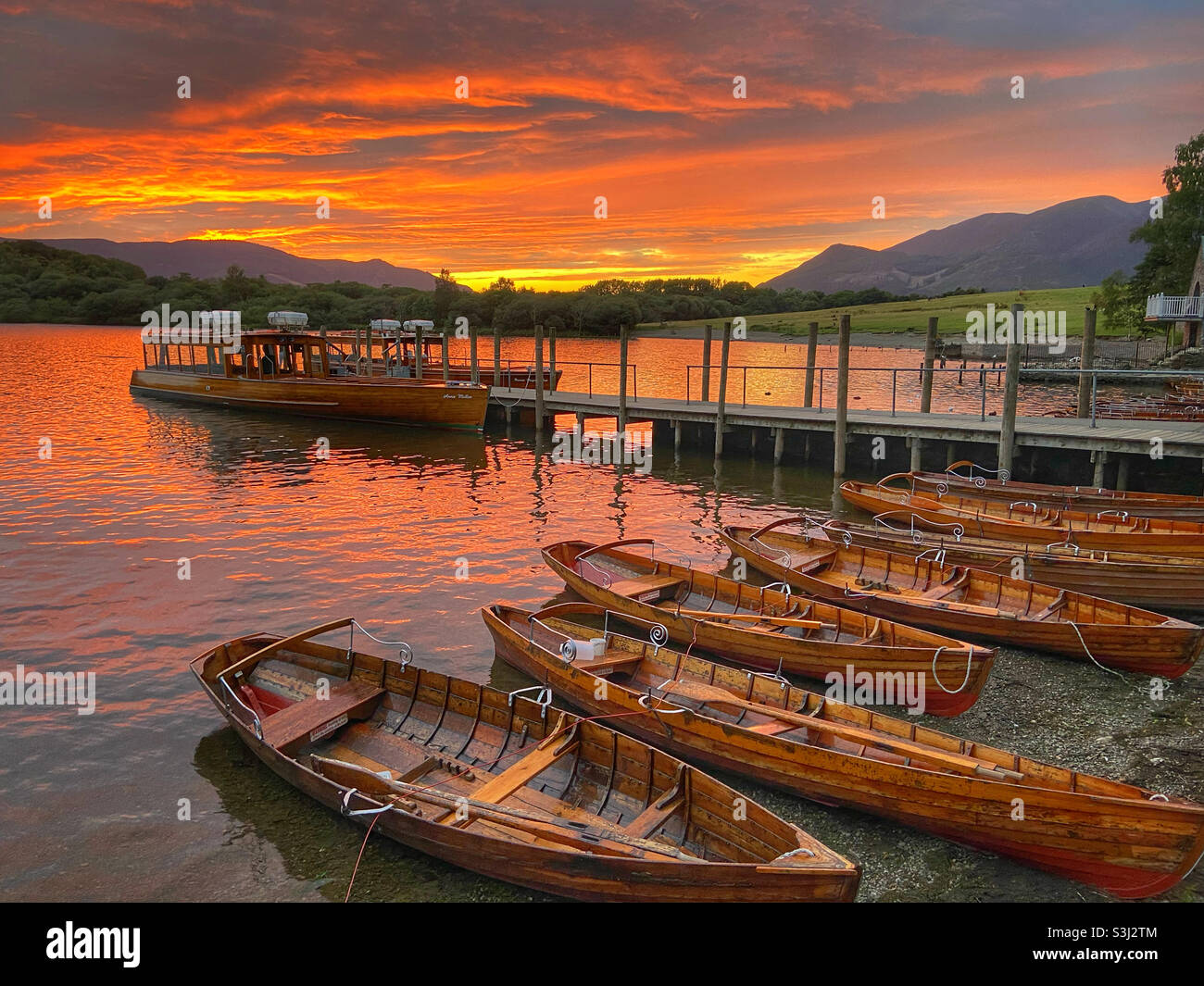 Ormeggiate barche a remi e traghetto a Keswick nel Lake District contro il tramonto del sole Foto Stock