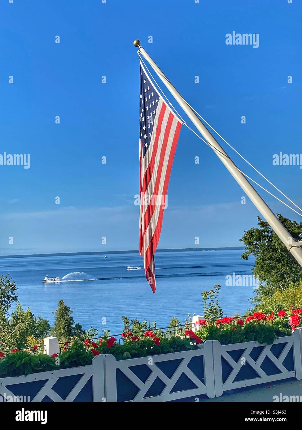 Bandiera americana vista dal ponte del Grand Hotel sull'isola di Mackinac. Il ponte Mackinac e il traghetto sono sullo sfondo Foto Stock