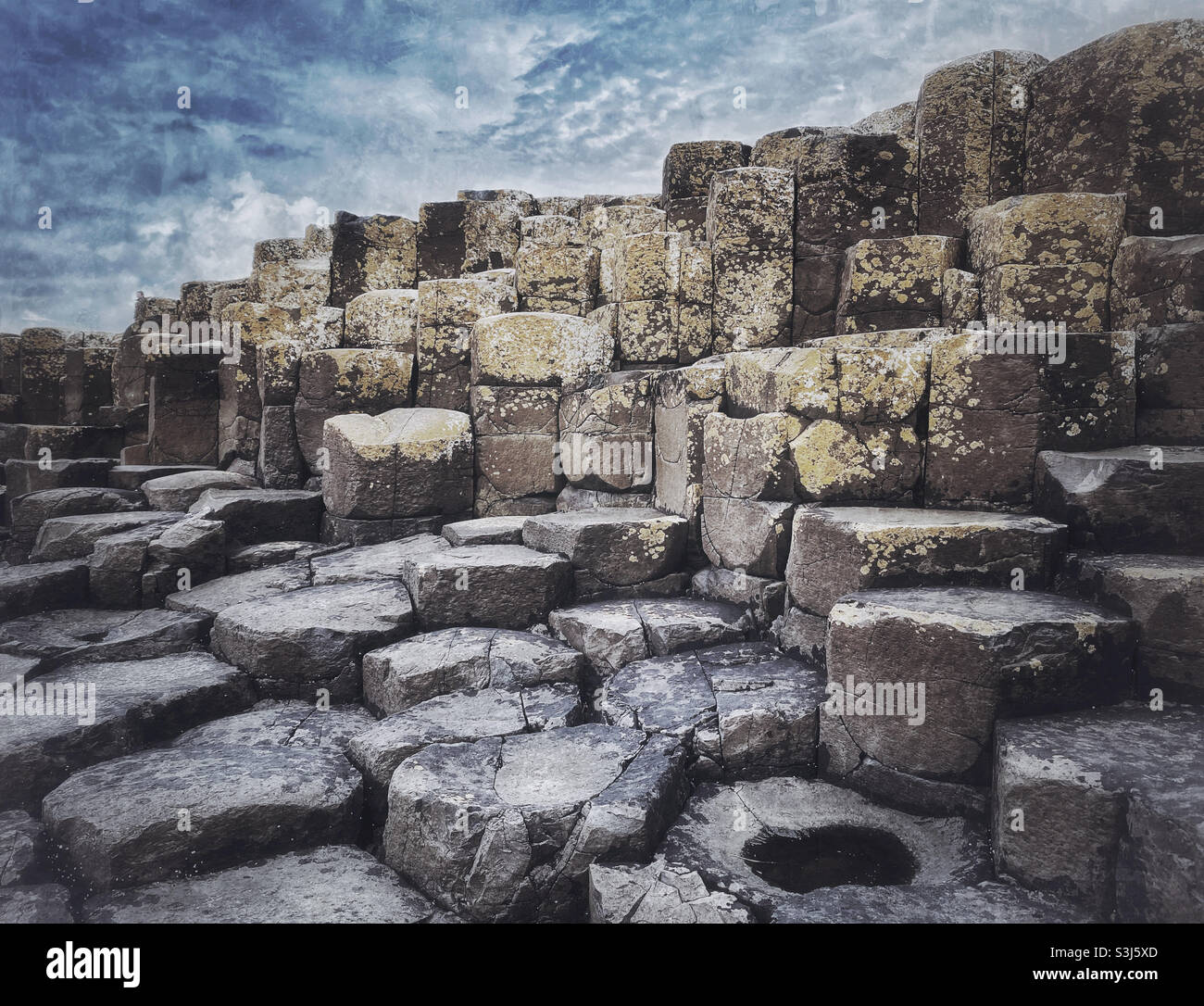 Un'immagine paesaggistica suggestiva delle colonne basaltiche che formano il fenomeno geologico noto come Selciato del Gigante. Queste strutture esagonali e pentagonali formate da eruzioni vulcaniche . ©️ C.HOSKINS. - Immagine stock catturata con smartphone
