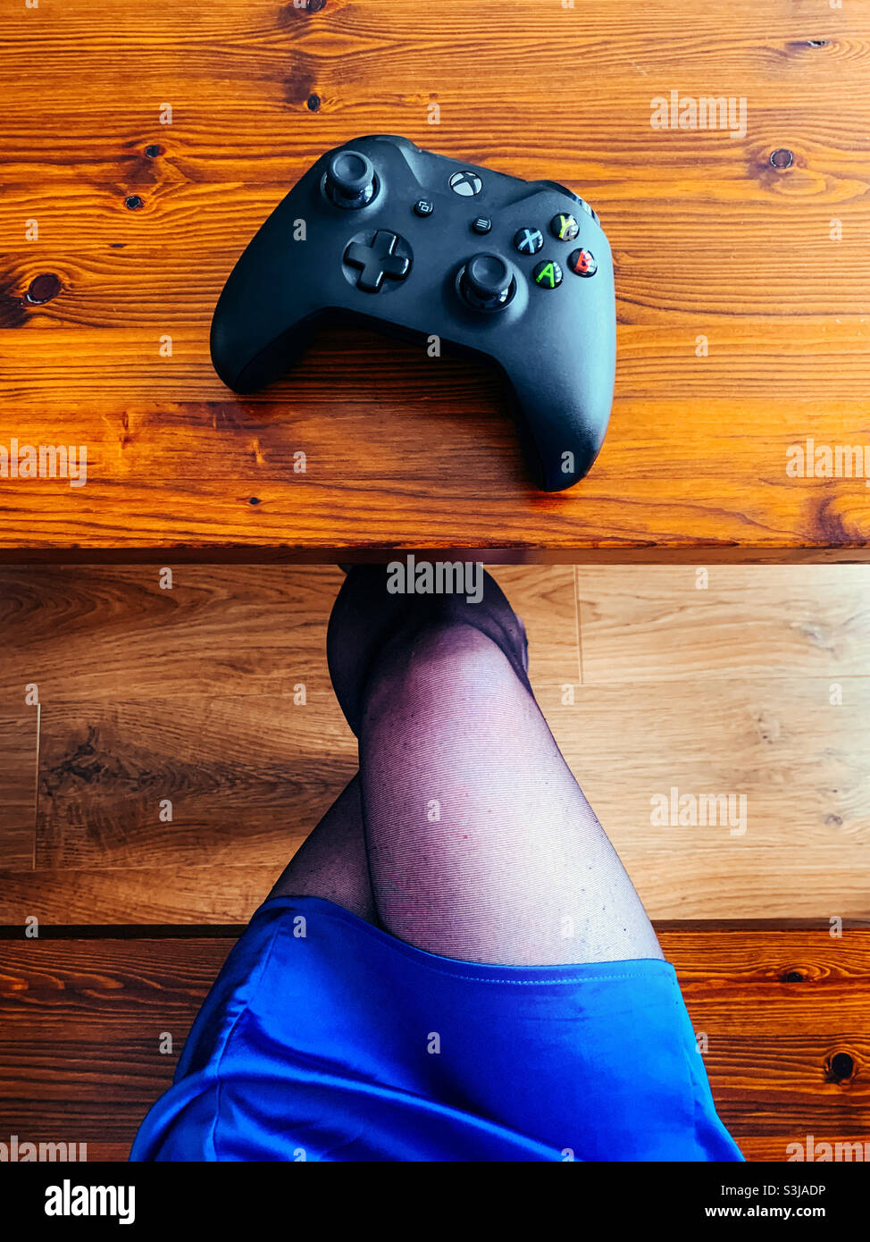 Controller di gioco Xbox su un tavolo di legno accanto a una donna con gambe incrociate Foto Stock