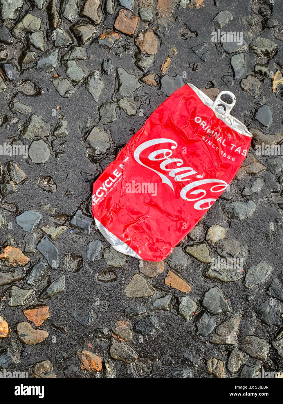 Una lattina schiacciata di gusto originale Coca-Cola è stata gettata sul lato di una strada. Questa bevanda è molto alta in zucchero e calorie. È spazzatura?! Foto ©️ COLIN HOSKINS. Foto Stock