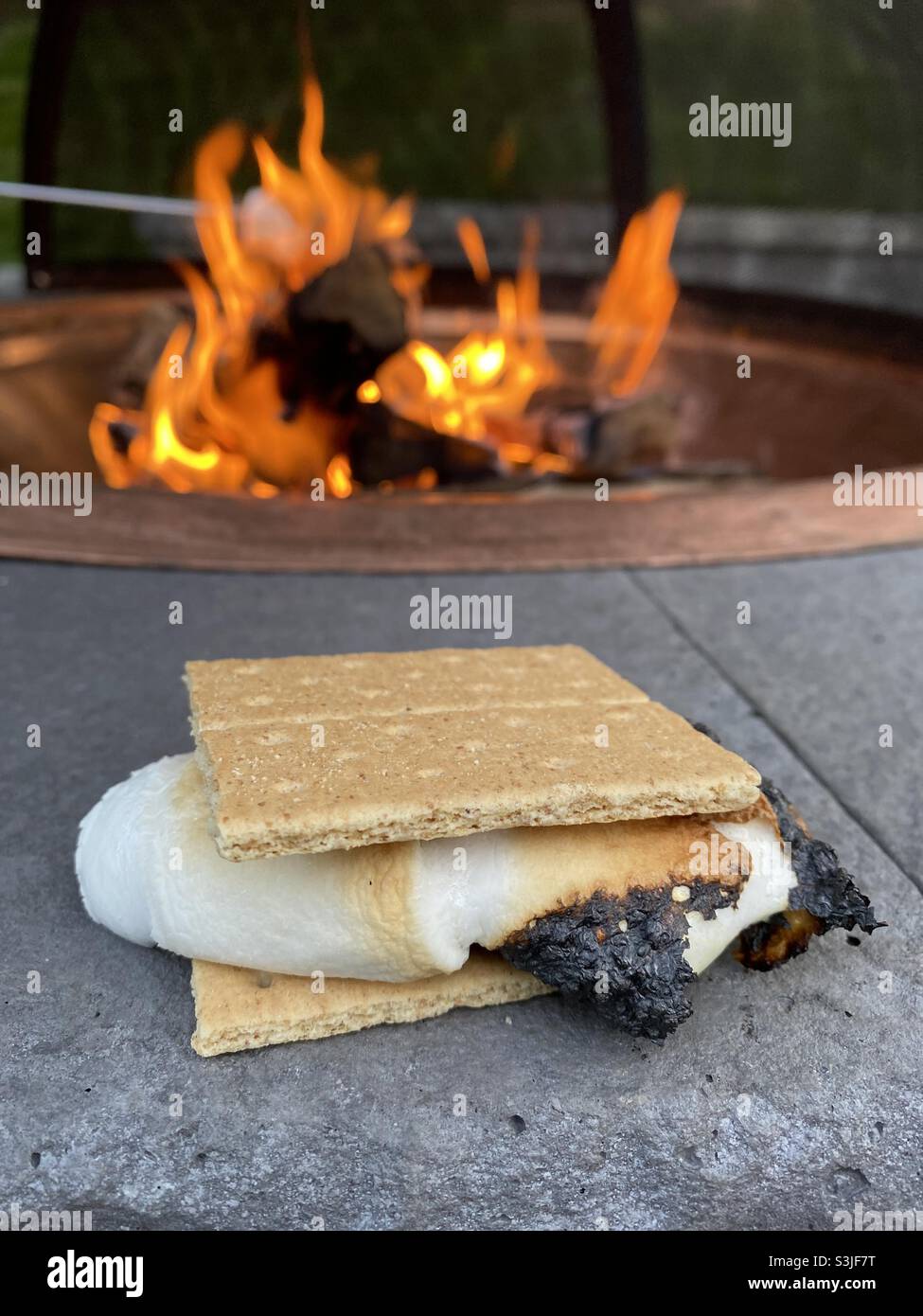 Ora! Un marshmallow croccante di melty arrostito viene fremito tra due cracker graham di fronte a una fossa di fuoco. Foto Stock