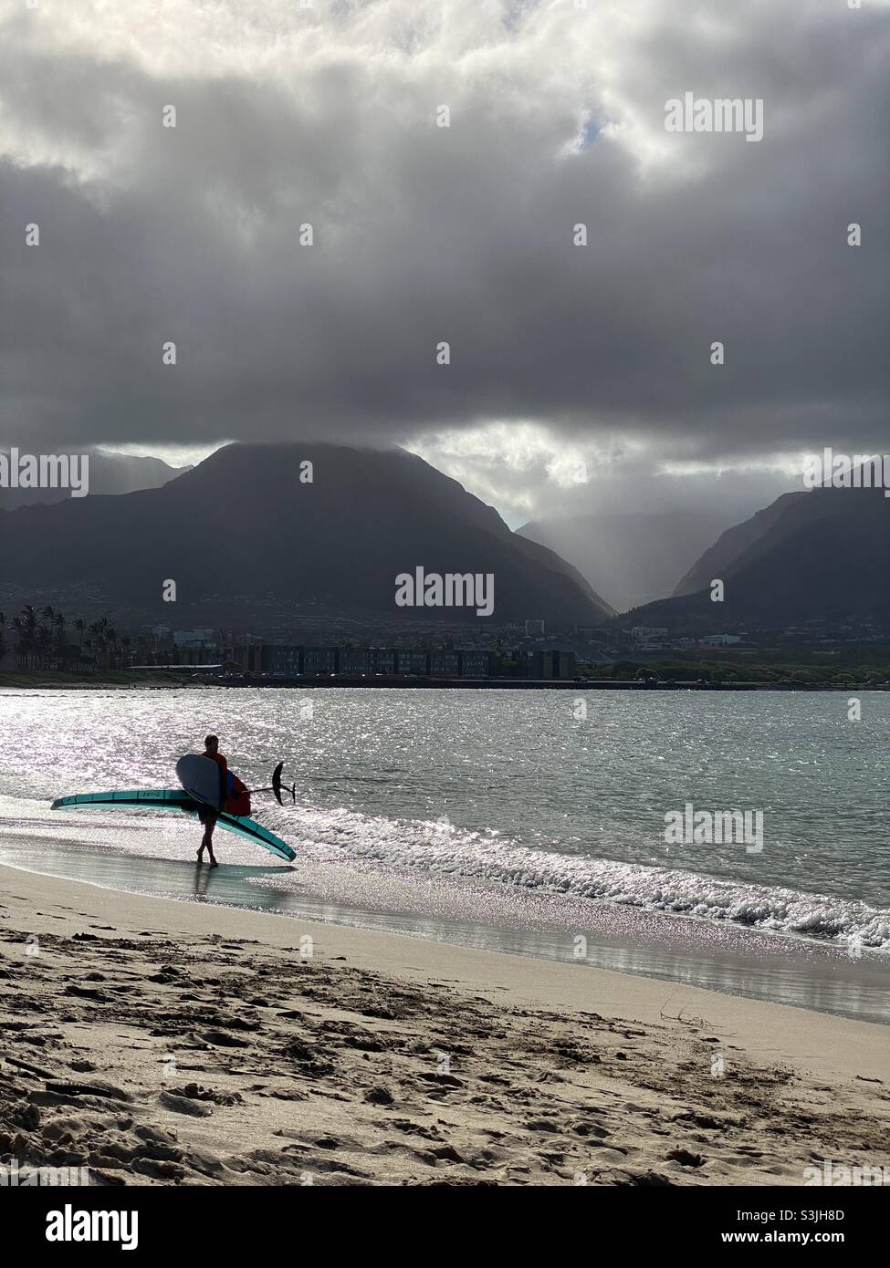 Uomo che gode di una tranquilla Moody Maui Beach giorno pronto a sorvolare l'ala Pacific Ocean surf. Foto Stock