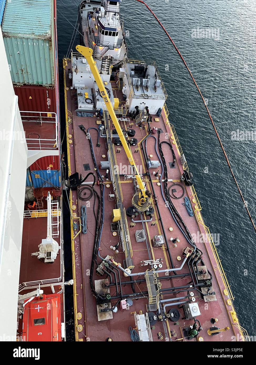 Chiatta bunker con rimorchiatore bianco accanto a un container mercantile durante l'operazione di bunkering, quando la nave da carico prende combustibile pesante nei loro serbatoi in terminal container nel porto commerciale del carico. Foto Stock