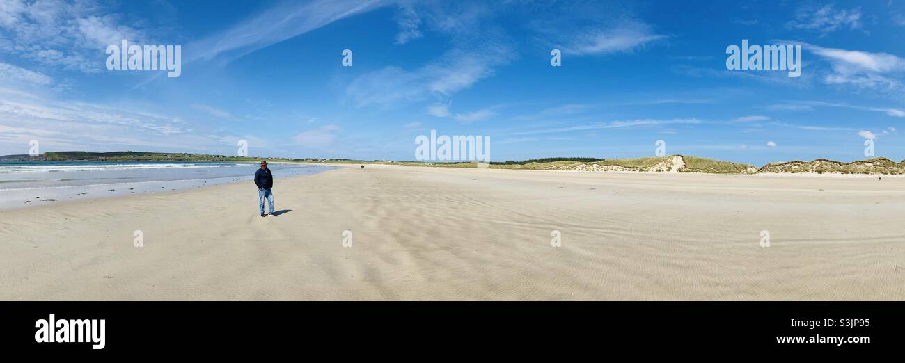 Uomo che cammina sulla spiaggia panoramica. Dunnett Bay sulla costa settentrionale 500. Scozia - Immagine stock catturata con smartphone