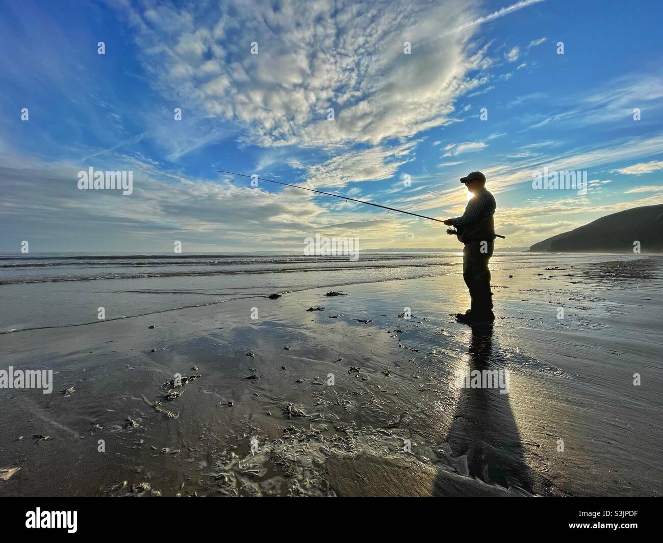 Lone pescatore su una spiaggia gallese al tramonto. Foto Stock