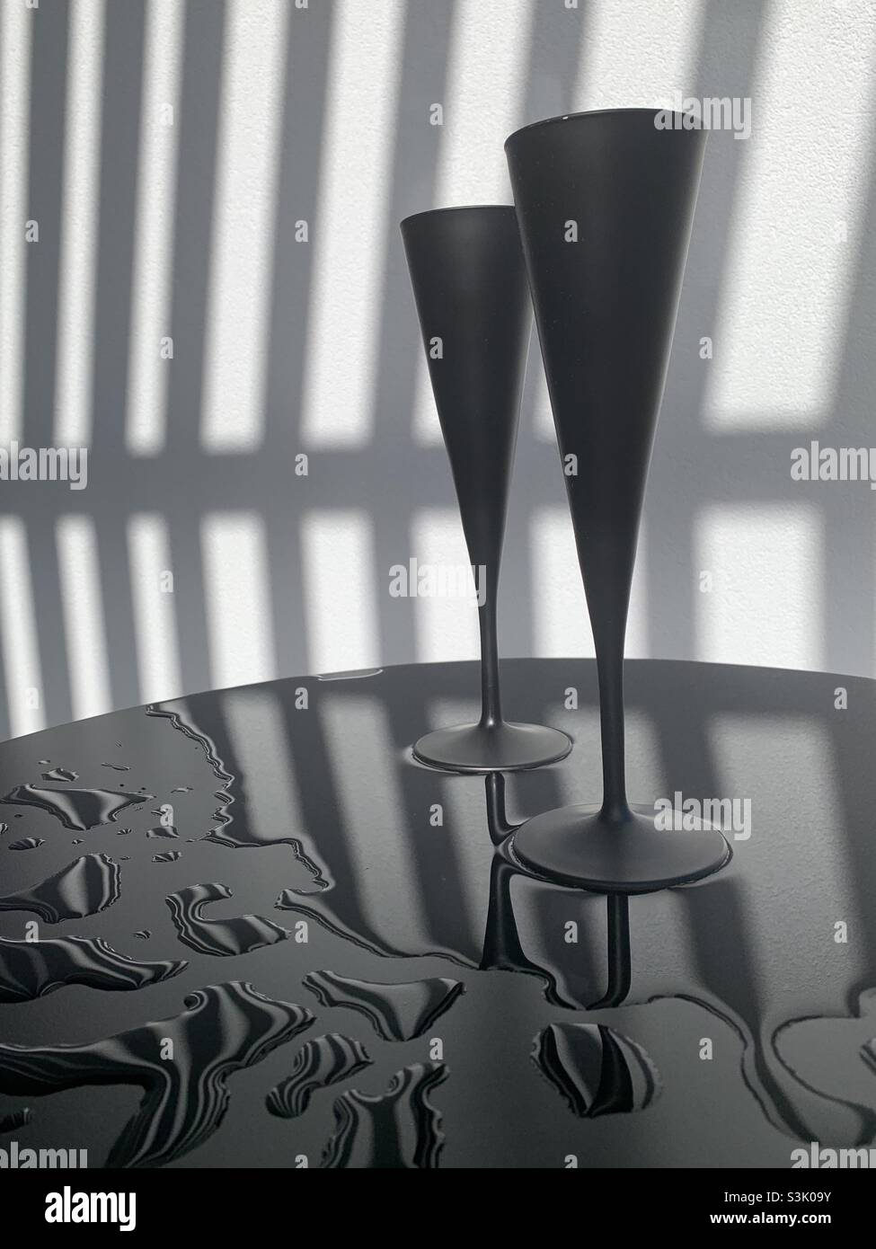 A champagne flute su un tavolo bagnato contro un muro ombreggiato Foto Stock