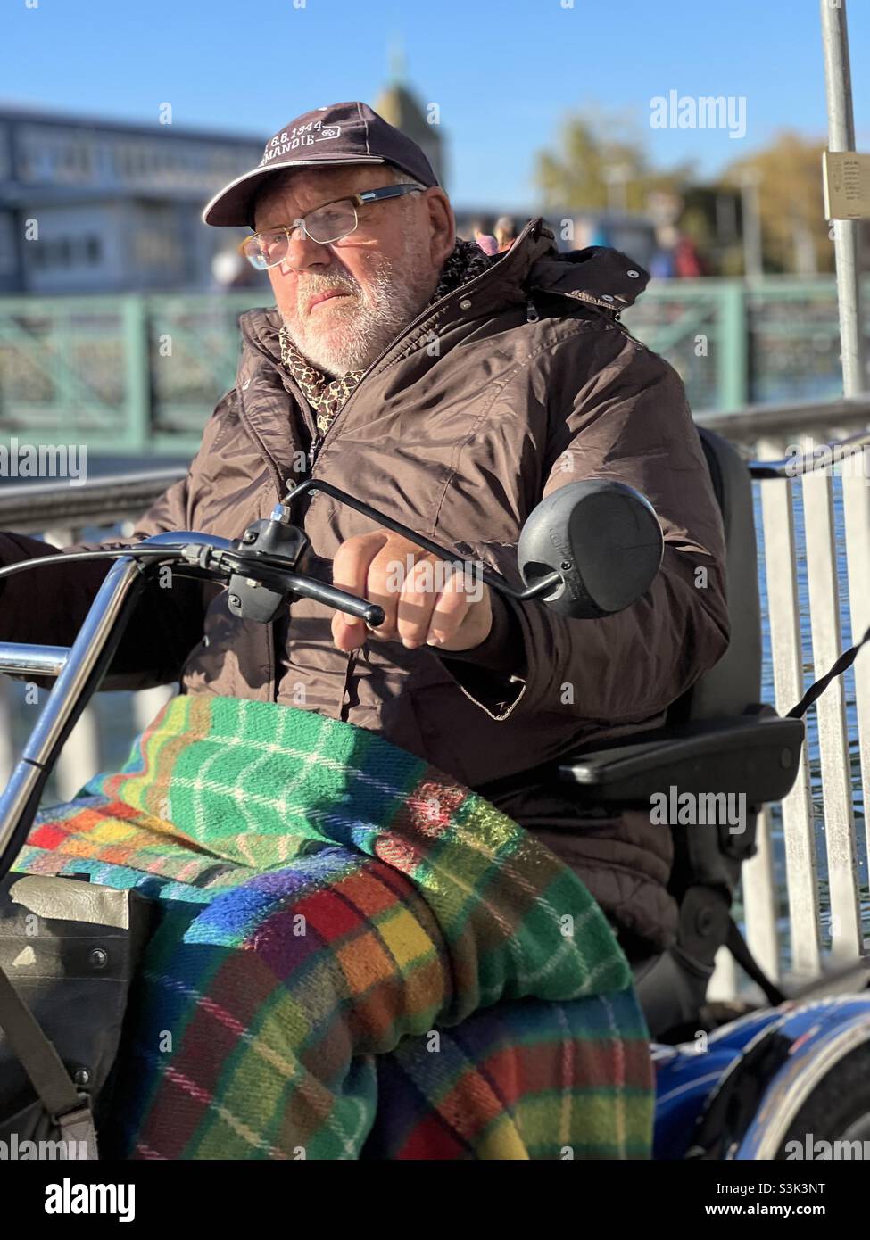 Uomo vecchio su una sedia a rotelle elettrica. Guida nel centro di Zurigo, in Svizzera, lungo il fiume Limmat. Il veicolo gli garantisce la mobilità e può superare la sua disabilità. Foto Stock