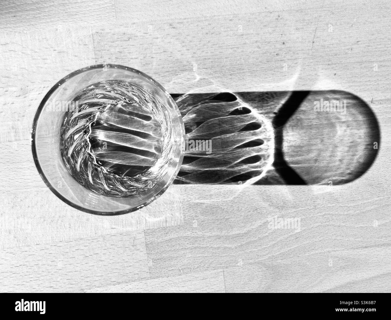 un bicchiere d'acqua si erge su un tavolo di legno e getta una lunga ombra Foto Stock