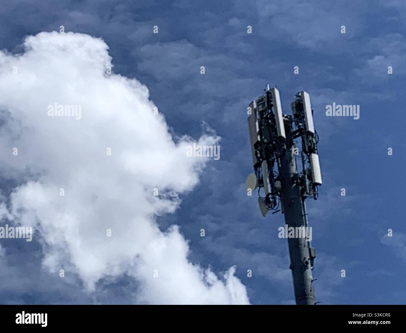 Una torre cellulare posta contro un cielo blu primaverile e nuvole incandescenti. - Immagine stock catturata con smartphone