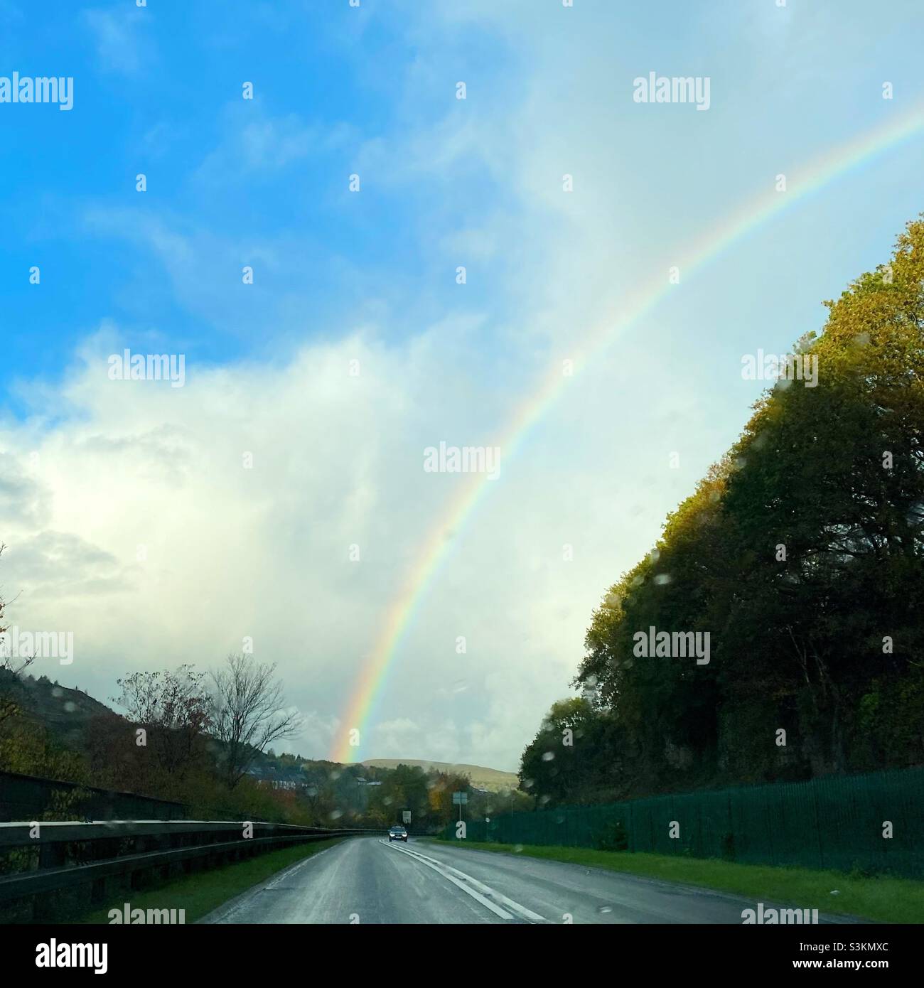 Una fotografia dall'interno di un'auto che guarda fuori in una giornata piovosa ad un arcobaleno e un veicolo in arrivo sulla strada Foto Stock
