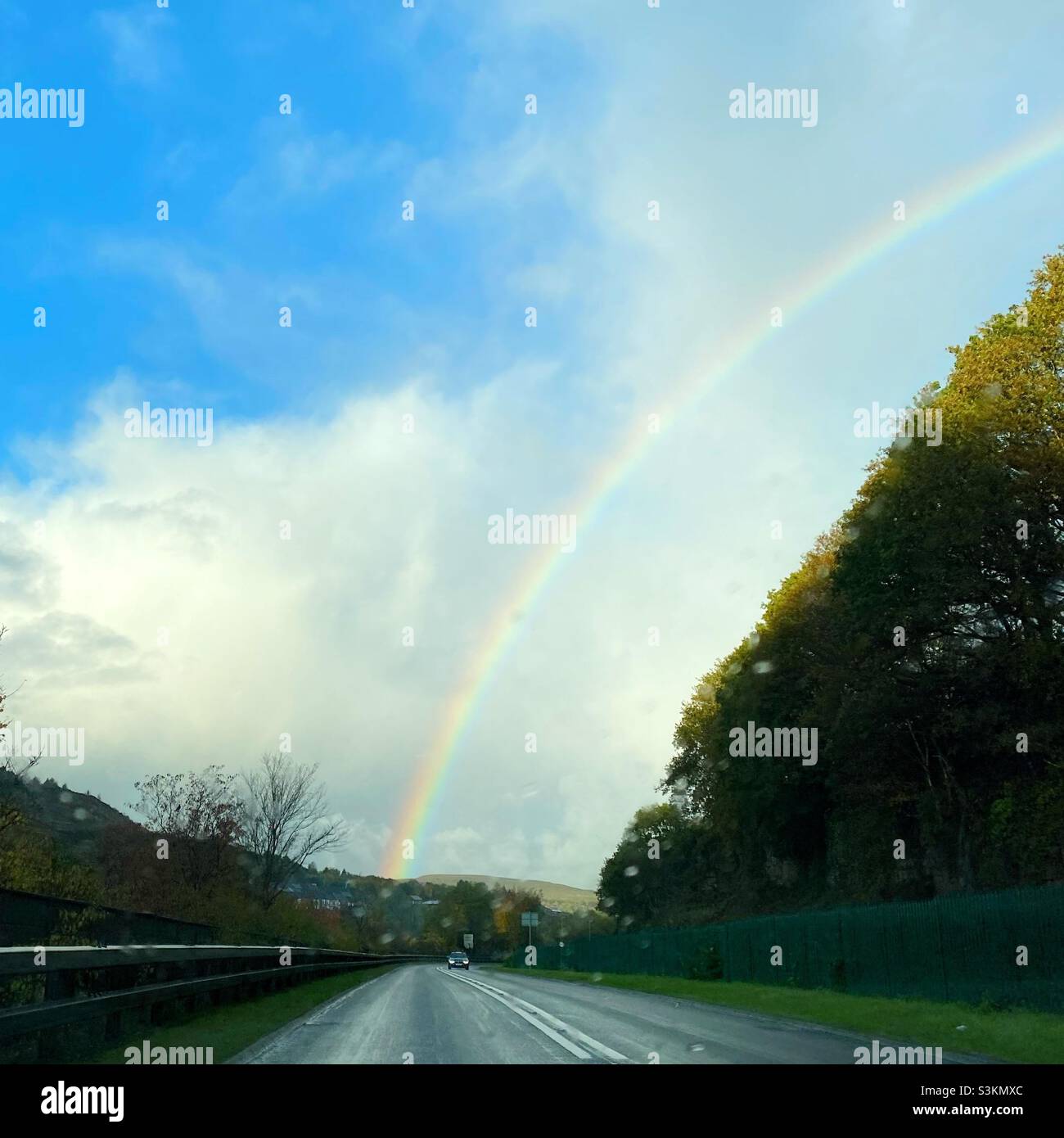 Una fotografia dall'interno di un'auto che guarda fuori in una giornata piovosa ad un arcobaleno e un veicolo in arrivo sulla strada - Immagine stock catturata con smartphone