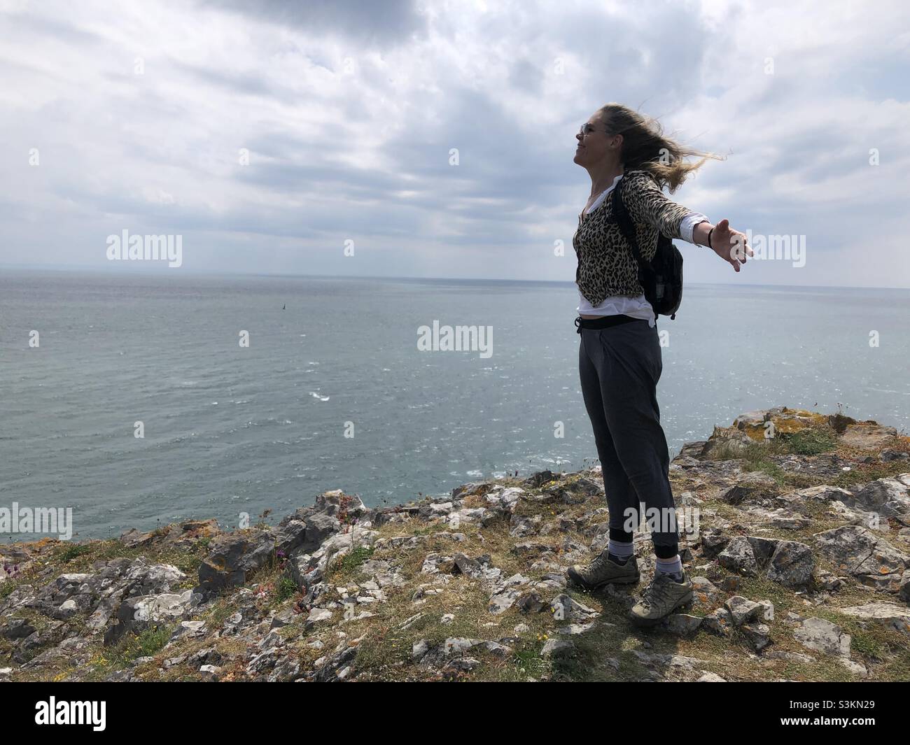 Una donna si alza con le braccia larghe di fronte ad un forte vento su una scogliera anche nel Galles del Sud Foto Stock