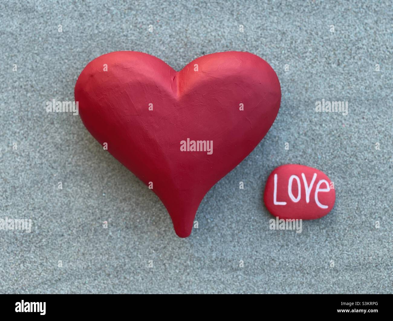 Concetto d'amore con un grande cuore di pietra rossa e una pietra intagliata fatta a mano con parola d'amore - Immagine stock catturata con smartphone