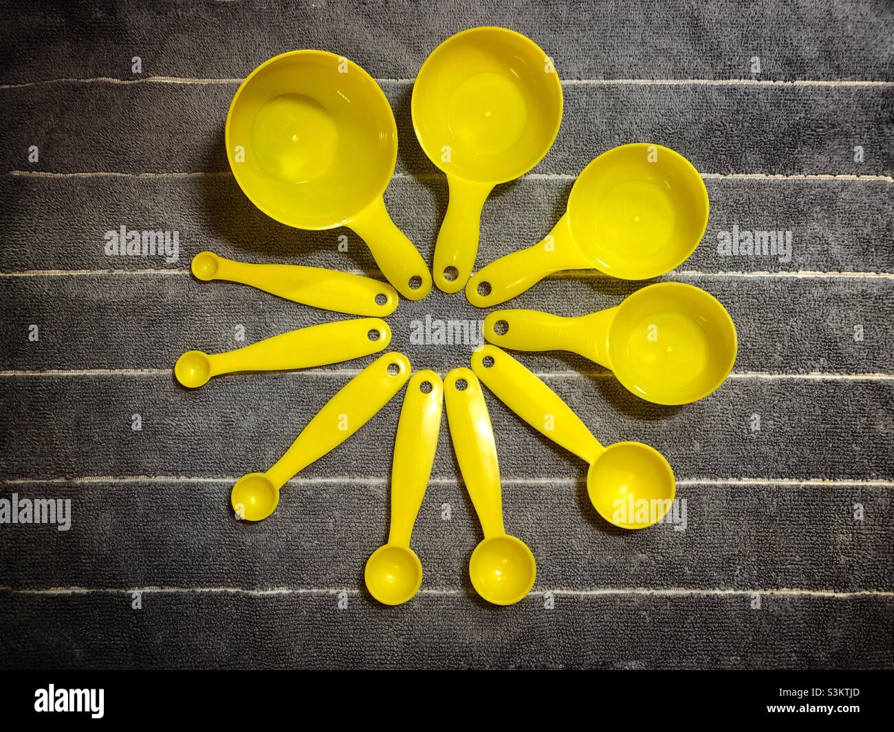 Misurini gialli, cucchiai e cucchiaini da tè su sfondo grigio. Foto Stock