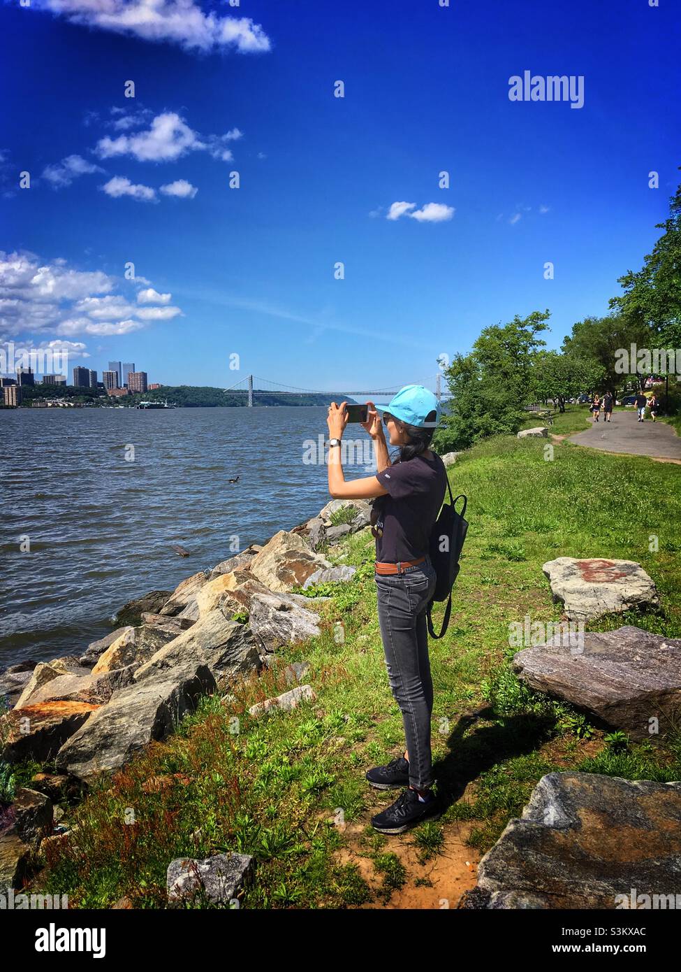 Una donna che fotografa, indossa un cappello blu cielo. In piedi al Riverside Park New York City. - Immagine stock catturata con smartphone