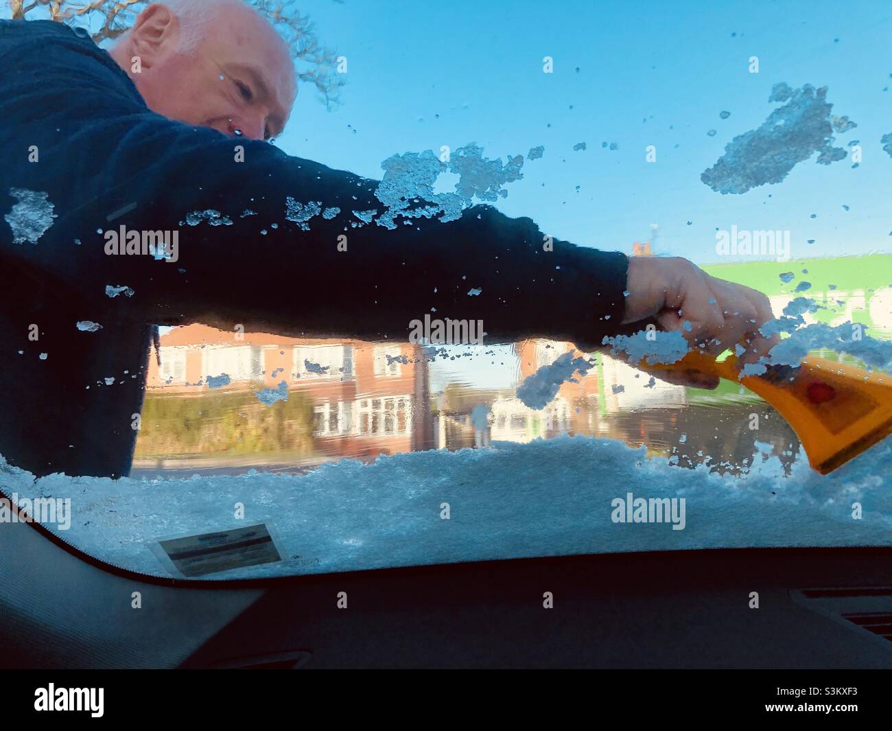 Uomo che sgombrano la neve da un parabrezza con un raschietto in plastica - Immagine stock catturata con smartphone