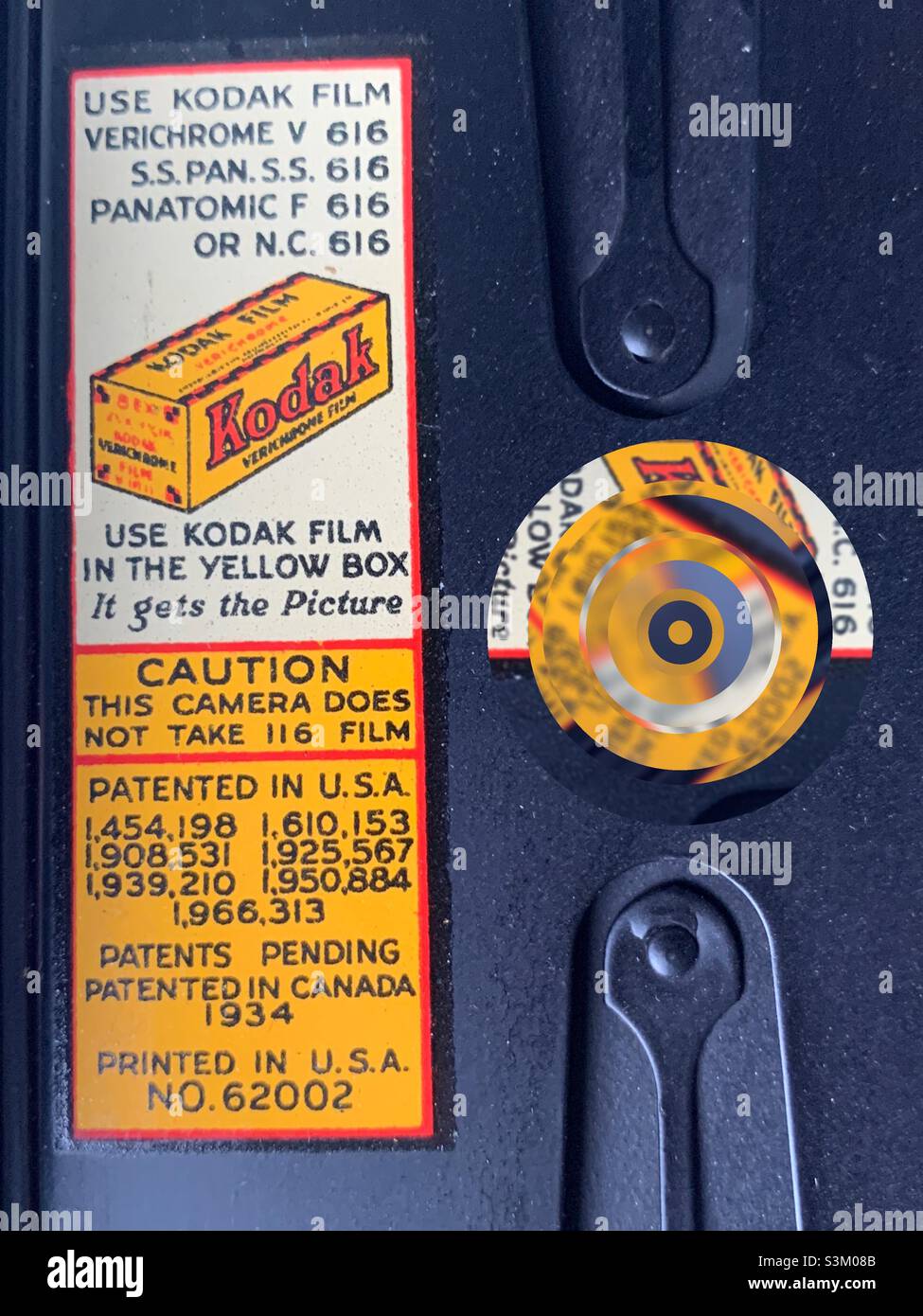 Etichetta Kodak (circa 1934) all'interno di questa fotocamera antica. Il cerchio prismatico e astratto sulla destra è stato aggiunto digitalmente e potrebbe rappresentare l’obiettivo, l’apertura, l’otturatore o l’anello di messa a fuoco di una telecamera. Foto Stock