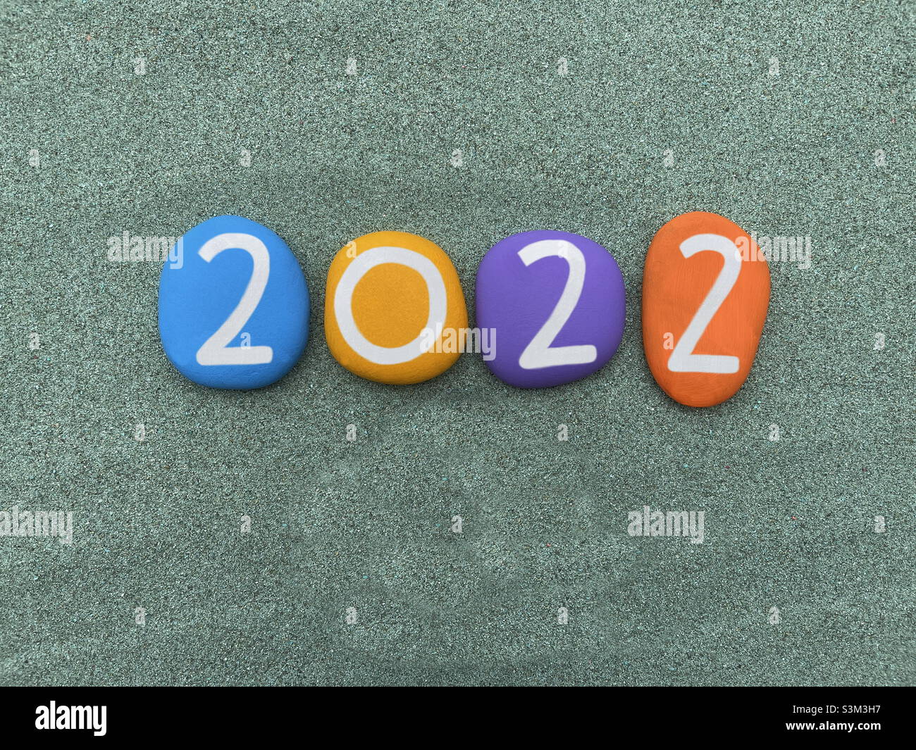 Anno 2022 composto con numeri di pietra dipinta a mano multicolore su sabbia verde - Immagine stock catturata con smartphone