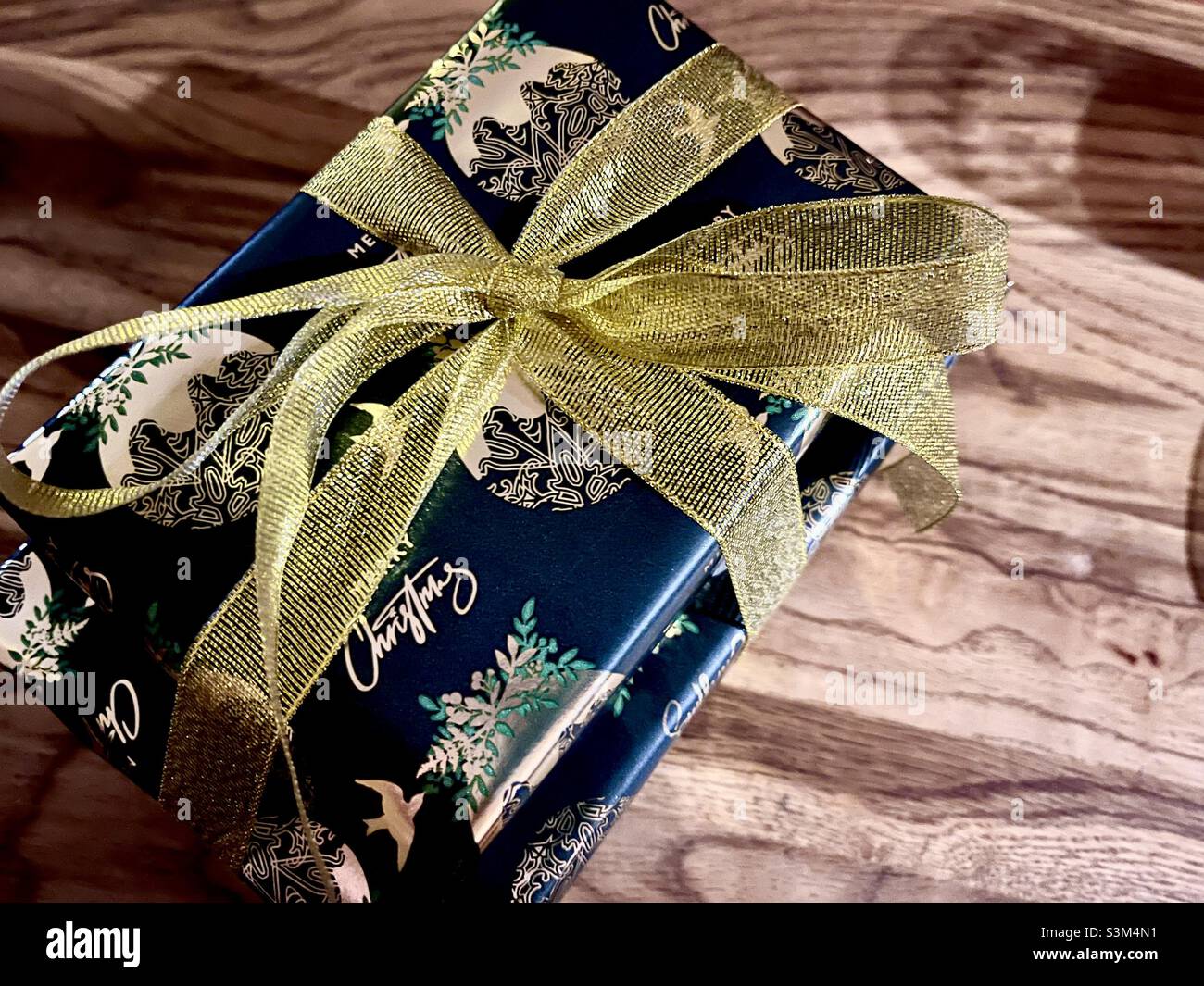 Regalo di Natale avvolto con un arco d'oro e posto sopra un tavolo di quercia con spazio copia Foto Stock