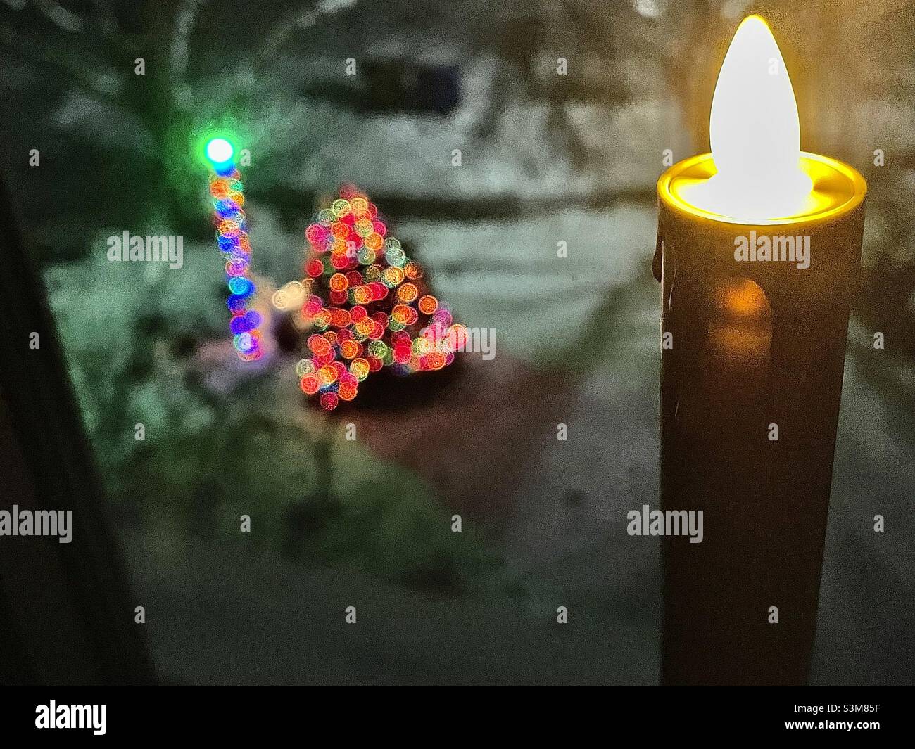 Una candela a batteria si illumina e sfarfalla nella finestra di una casa al piano superiore, guardando fuori nel loro cortile con le luci di Natale splendente in Utah, Stati Uniti. - Immagine stock catturata con smartphone