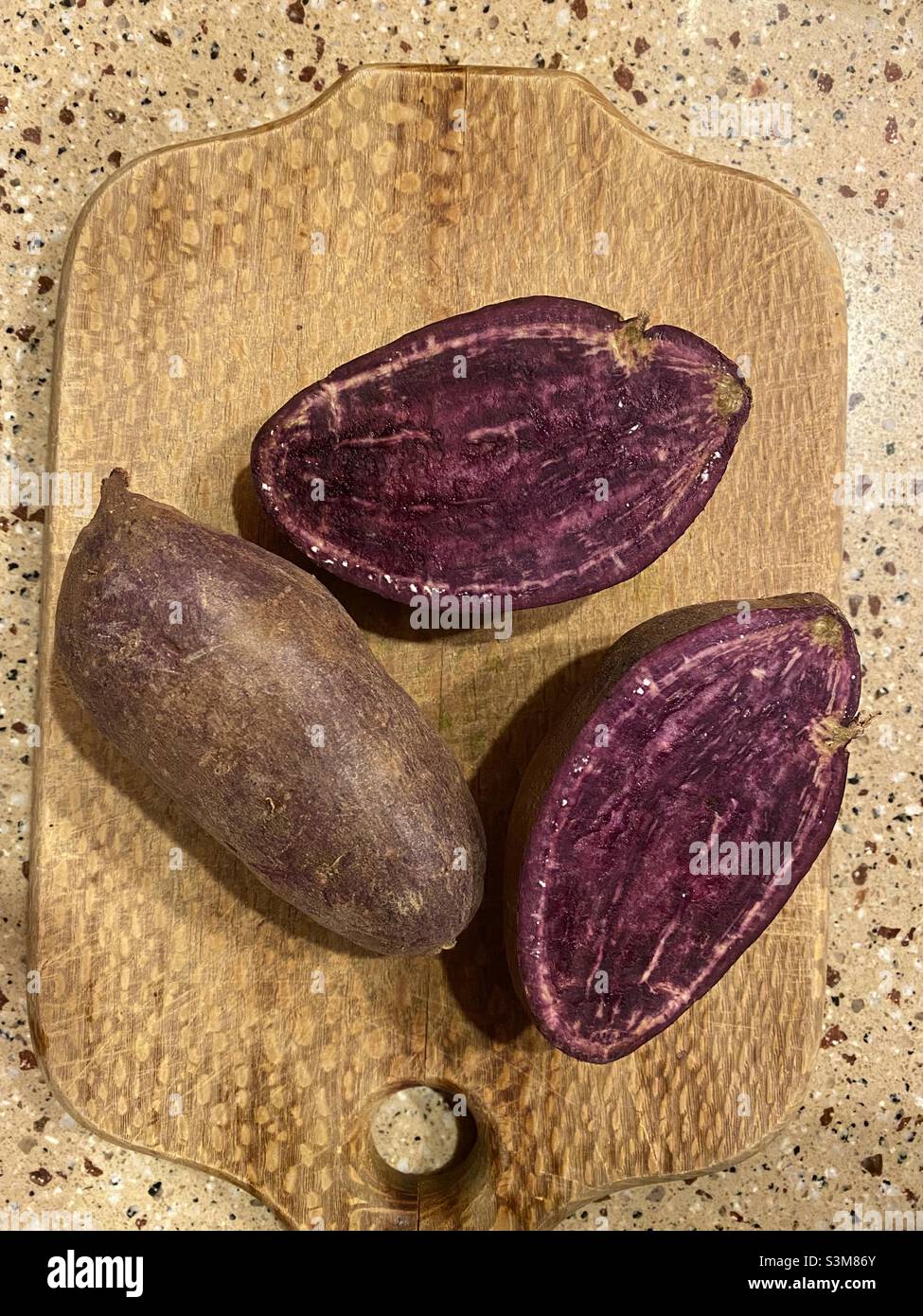 Patate dolci viola su un tagliere in cucina. Foto Stock