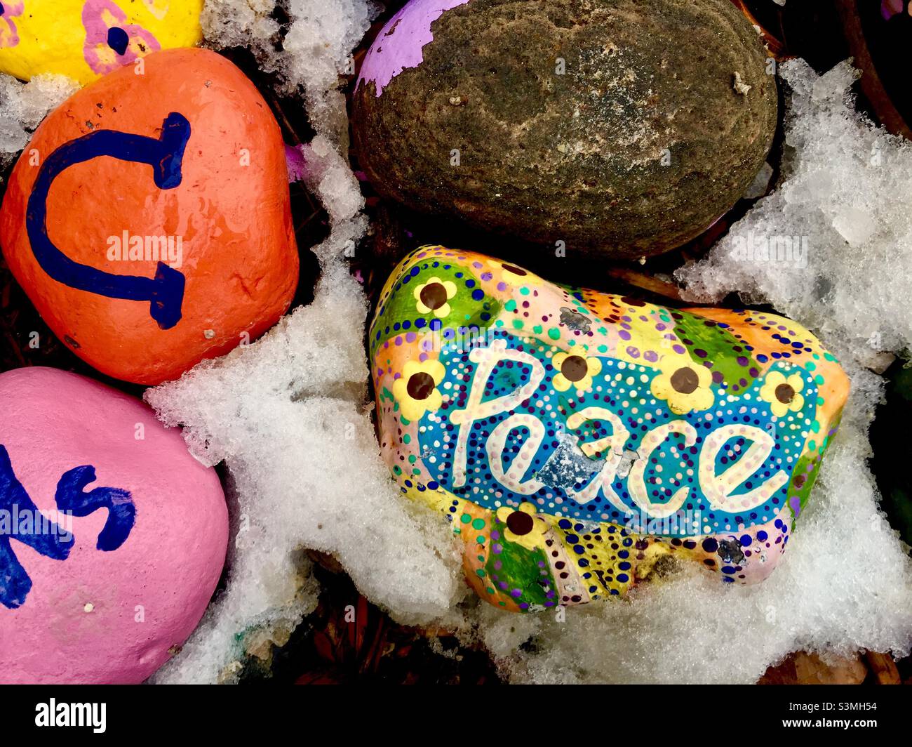 Pace e altri simboli dipinti su pietre, all'aperto, sdraiati nella neve fresca, Ontario, Canada. Dipinti, spesso eseguiti da bambini, o come terapia d'arte per problemi di salute mentale. Foto Stock