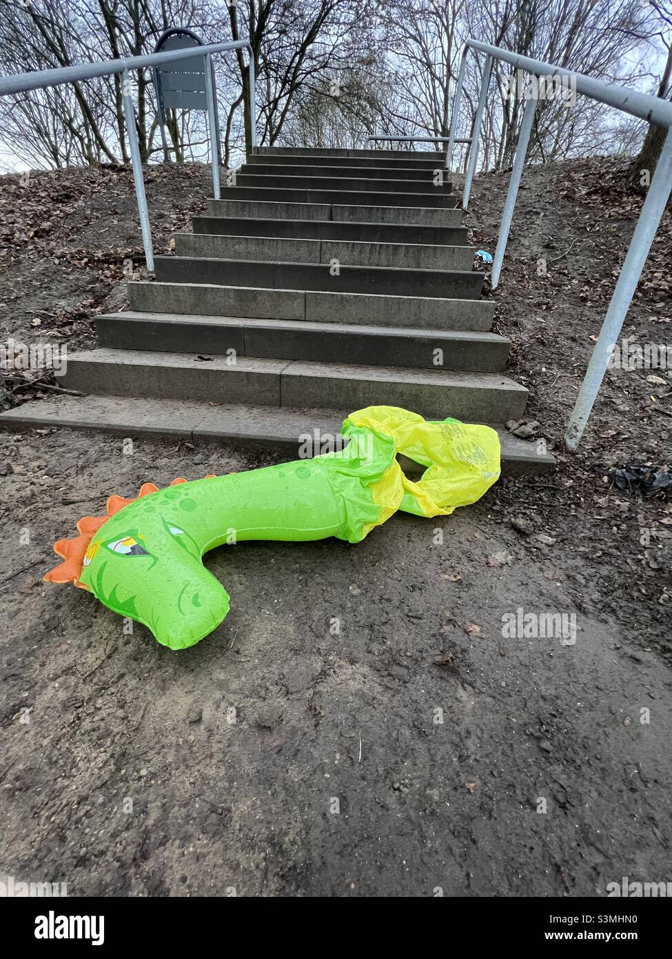 Un giocattolo gonfiabile verde - un dinosauro o un drago - abbandonato, danneggiato, in fondo alle scale a terra. Una triste storia di essere lasciato, ferito, perso. Foto Stock