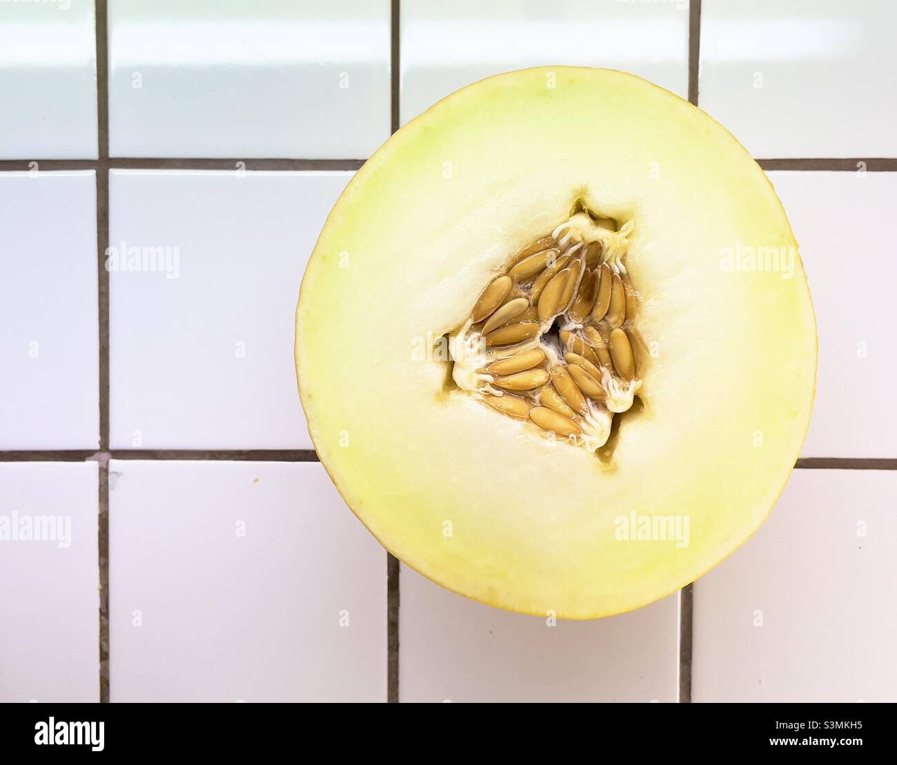 Un melone di mezzo canarino che mostra i semi al centro, poggiando su un piano di lavoro piastrellato di bianco. Foto Stock