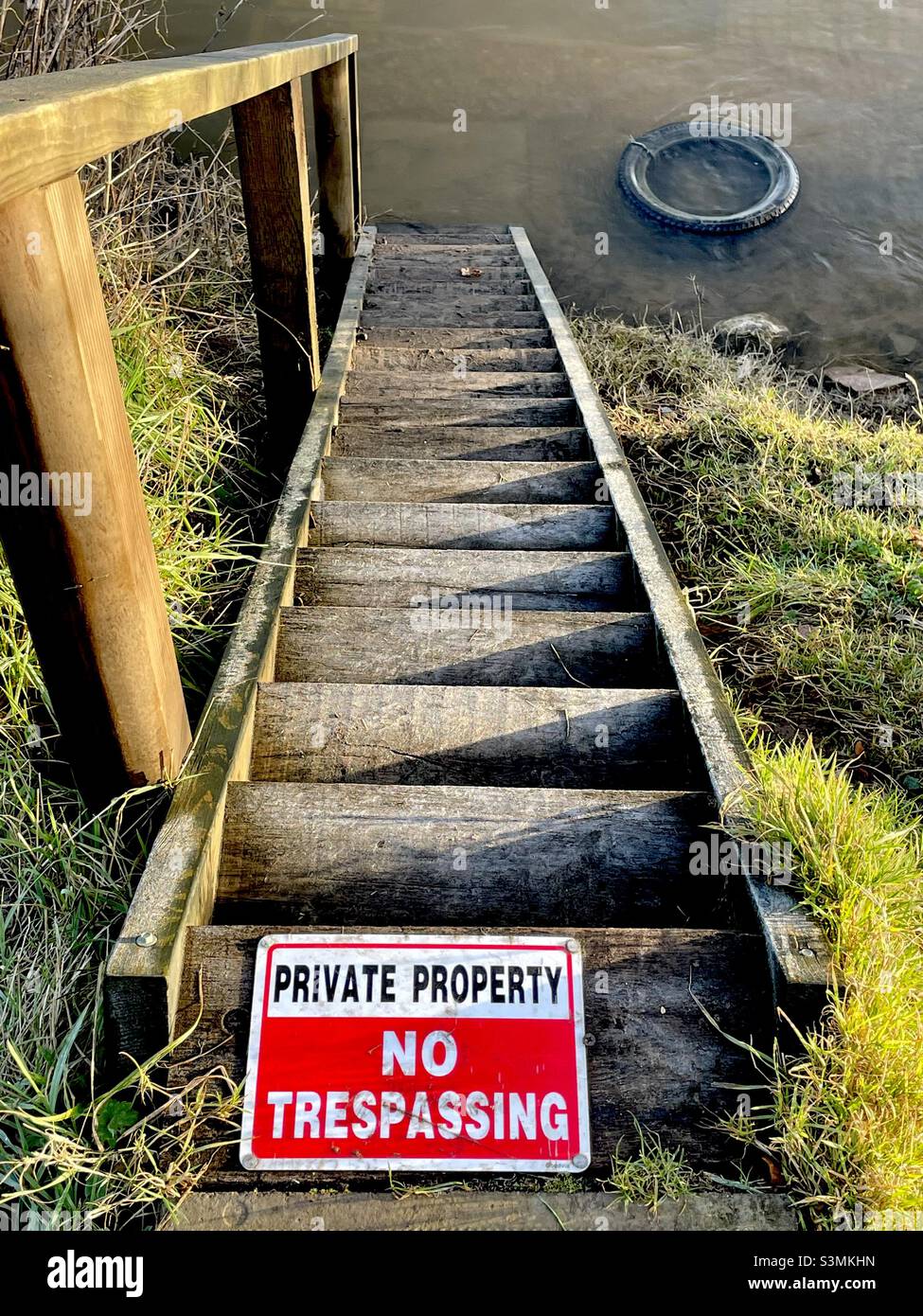 Una scalinata di legno che scende fino ad un ormeggio sul fiume Severn, con un avviso che dice “no trespassing” - Immagine stock catturata con smartphone