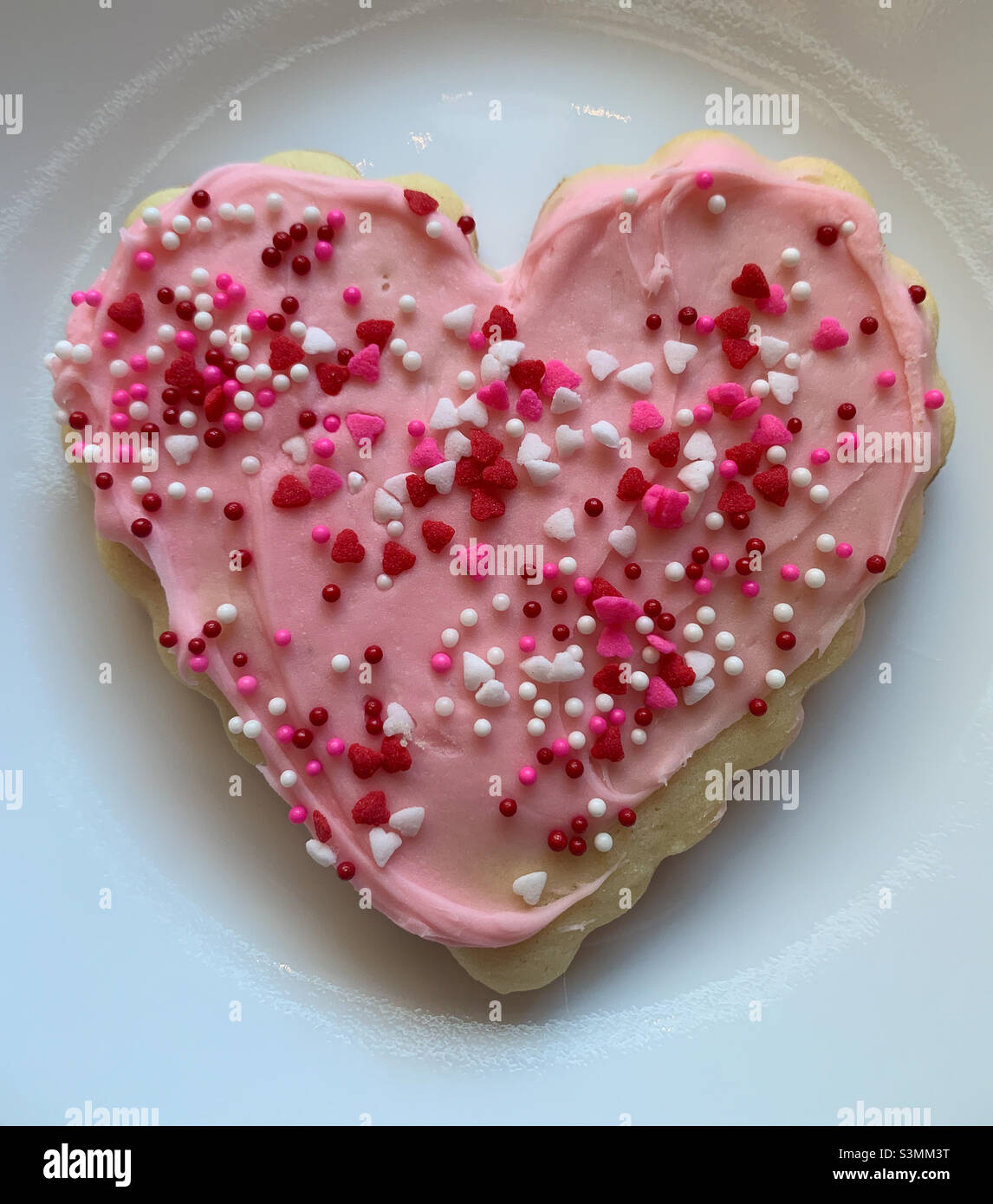 Biscotto a forma di cuore con glassa rosa e spolverini di cuore per San Valentino. Foto Stock