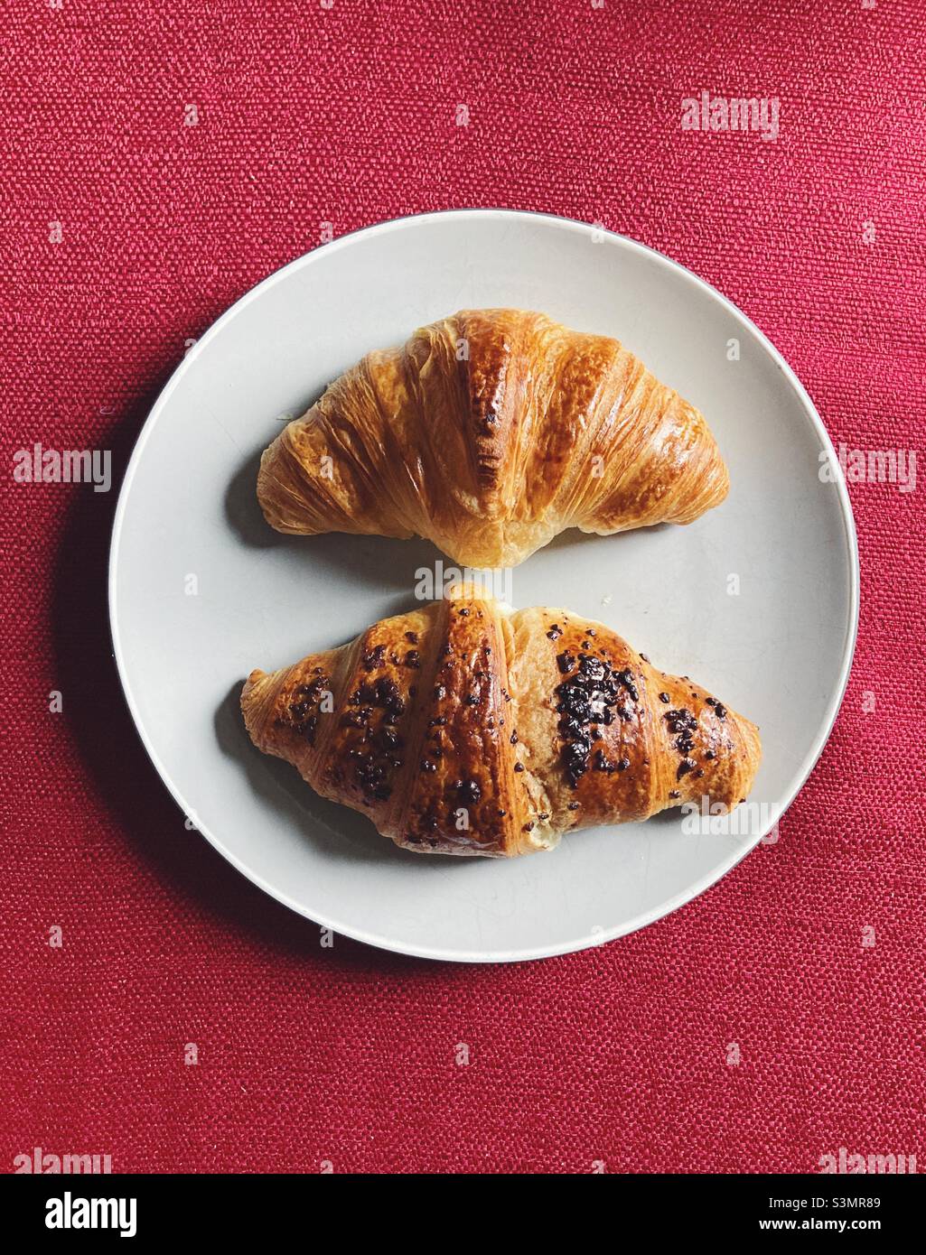 Un croissant al cioccolato e un croissant al cioccolato su un piatto su una tovaglia di panno rosso Foto Stock