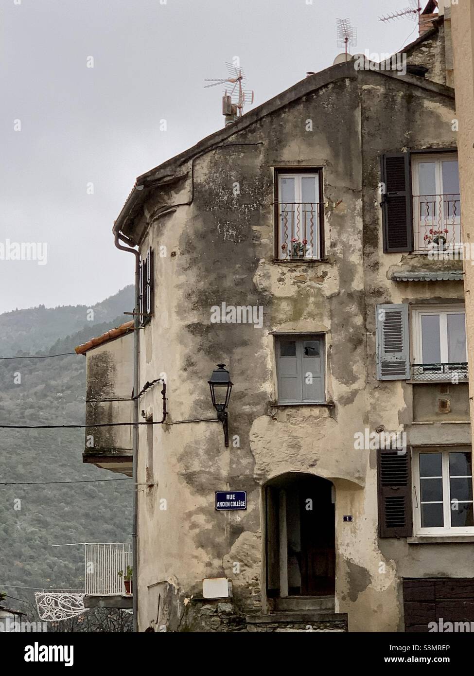 Corte, Corsica. Casa alta e fatiscente con vista sulle montagne davanti e porta con gradini. Rue Ancien Collège. Foto Stock