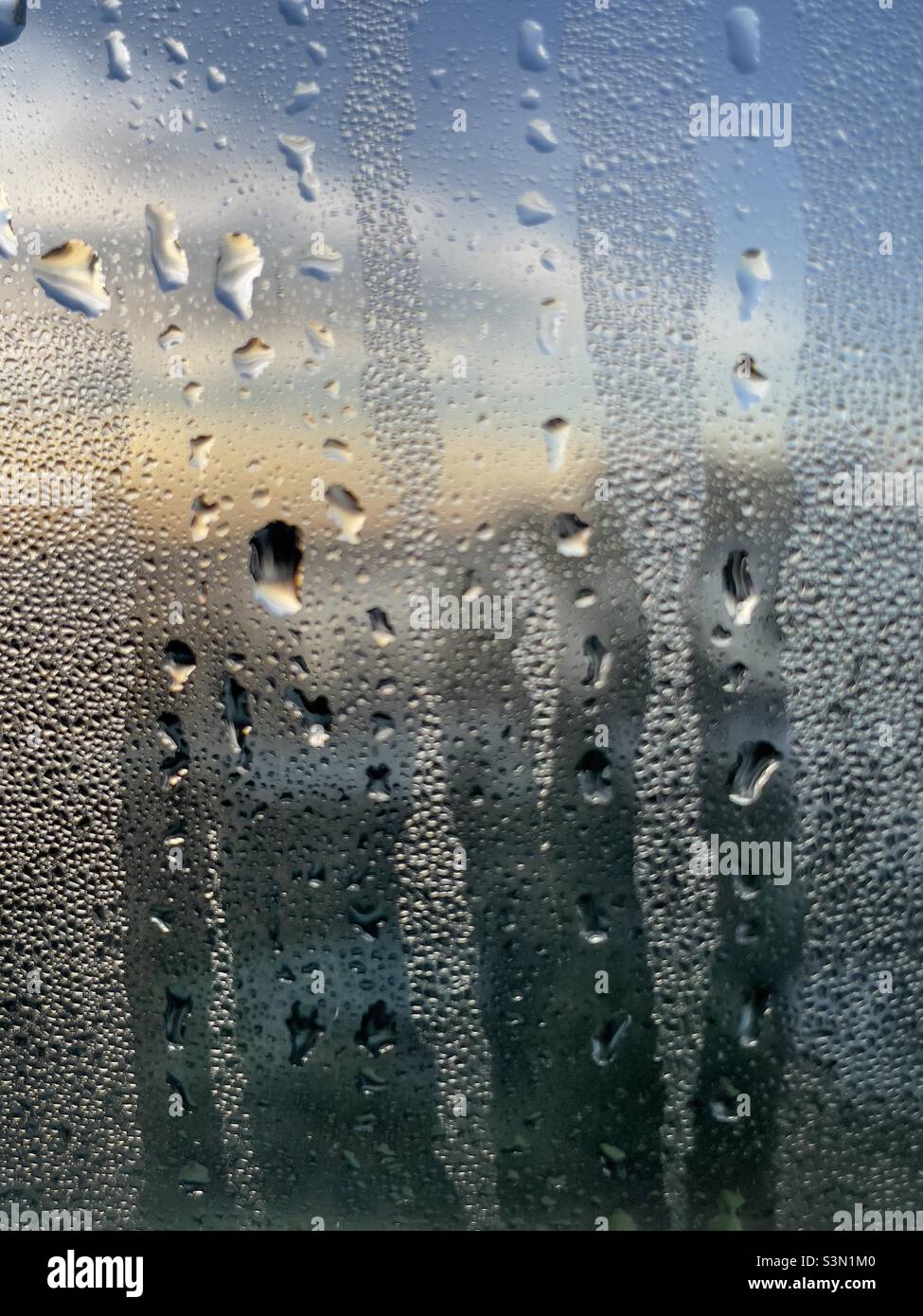 Goccioline d'acqua e goccioline su una finestra, ricoperta di condensa, di fronte al cielo dell'alba - Immagine stock catturata con smartphone