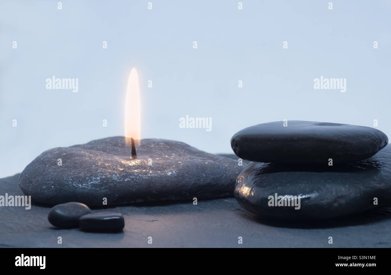Immagine blu/grigia di ciottoli di fiume lisci e una candela Foto Stock