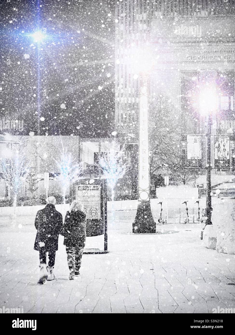 Un paio di amici che camminano a nord fuori dal City Creek Center nel centro di Salt Lake City, Utah, USA. Attraverso la tempesta di neve aggiunta digitalmente, è possibile vedere la sede della Chiesa LDS e l'edificio degli uffici - Immagine stock catturata con smartphone