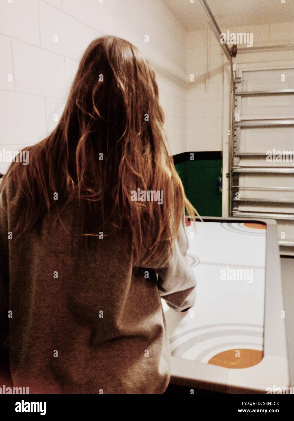 Ragazza con i capelli lunghi che gioca l'hockey dell'aria nel garage Foto Stock