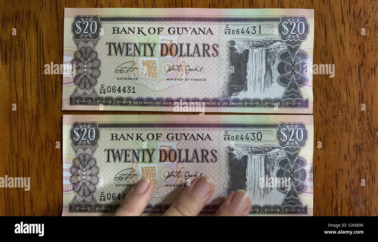 Mano su due banconote del ventiduesimo dollaro guyanese. Cubani in Guyana. Georgetown, Guyana. - Immagine stock catturata con smartphone