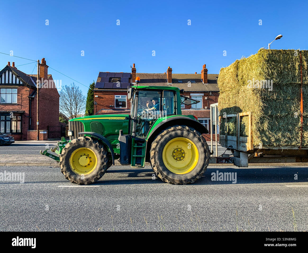 John Deere 6920S inseguitore di utilità e balle di fieno che attraversano il villaggio Foto Stock