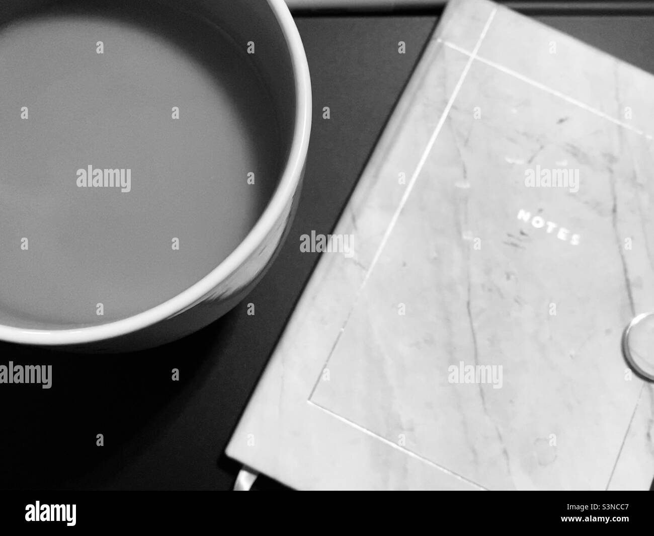 Notebook chiuso etichettato "Notes" e una grande tazza di caffè su una scrivania nera in bianco e nero, preparazione per la riunione, il lavoro da casa, scuola virtuale Foto Stock