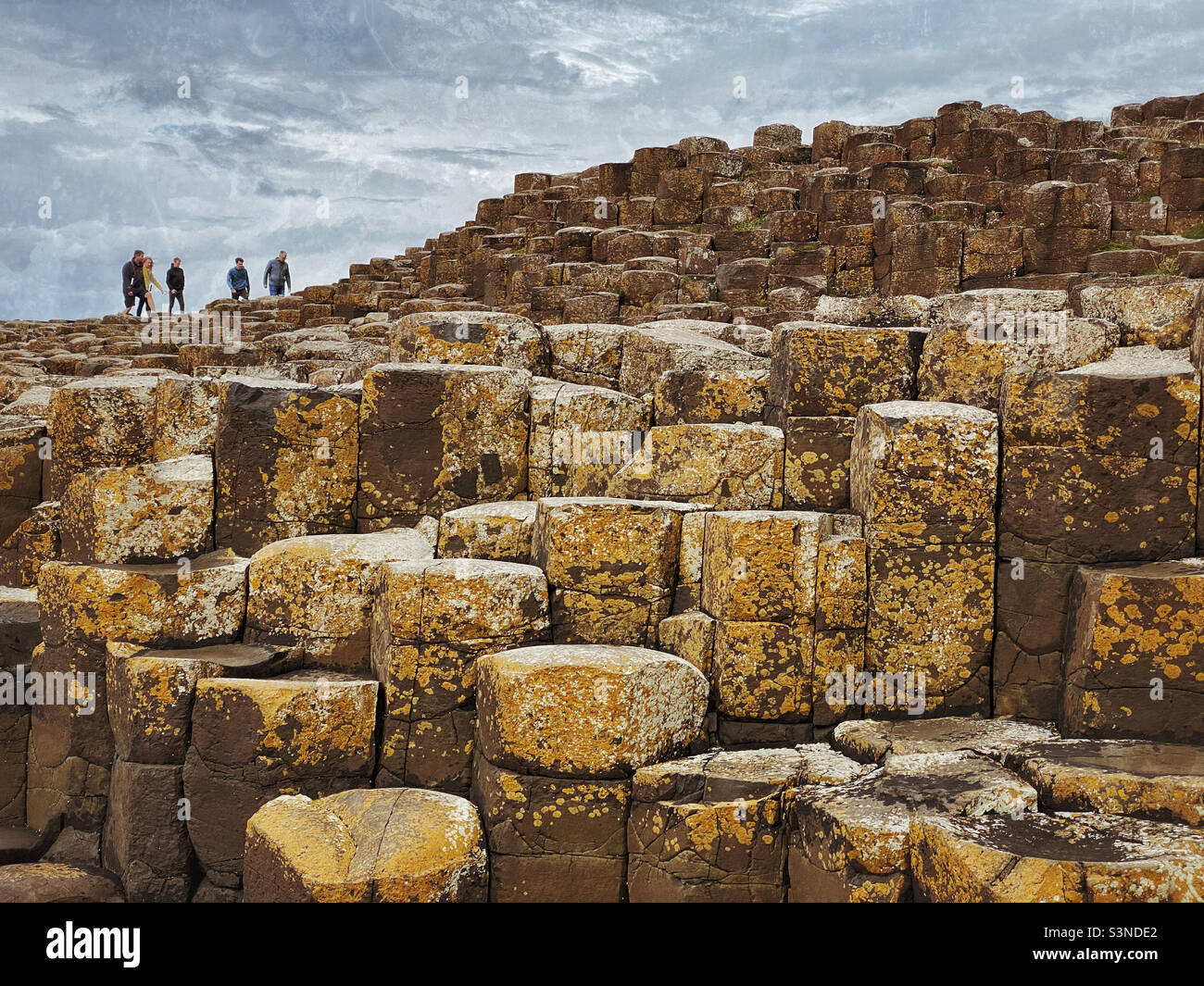 I turisti/visitatori camminano sulle uniche formazioni rocciose di basalto che formano l'area conosciuta come Selciato del Gigante ad Antrim, Irlanda del Nord. Le strutture esagonali sono state formate 60 milioni di anni fa. ©️ CH Foto Stock