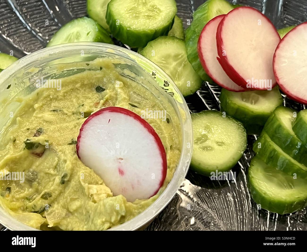 Spuntino di fette di cetriolo e ravanelli con una tazza da una tazza di guacamole Foto Stock