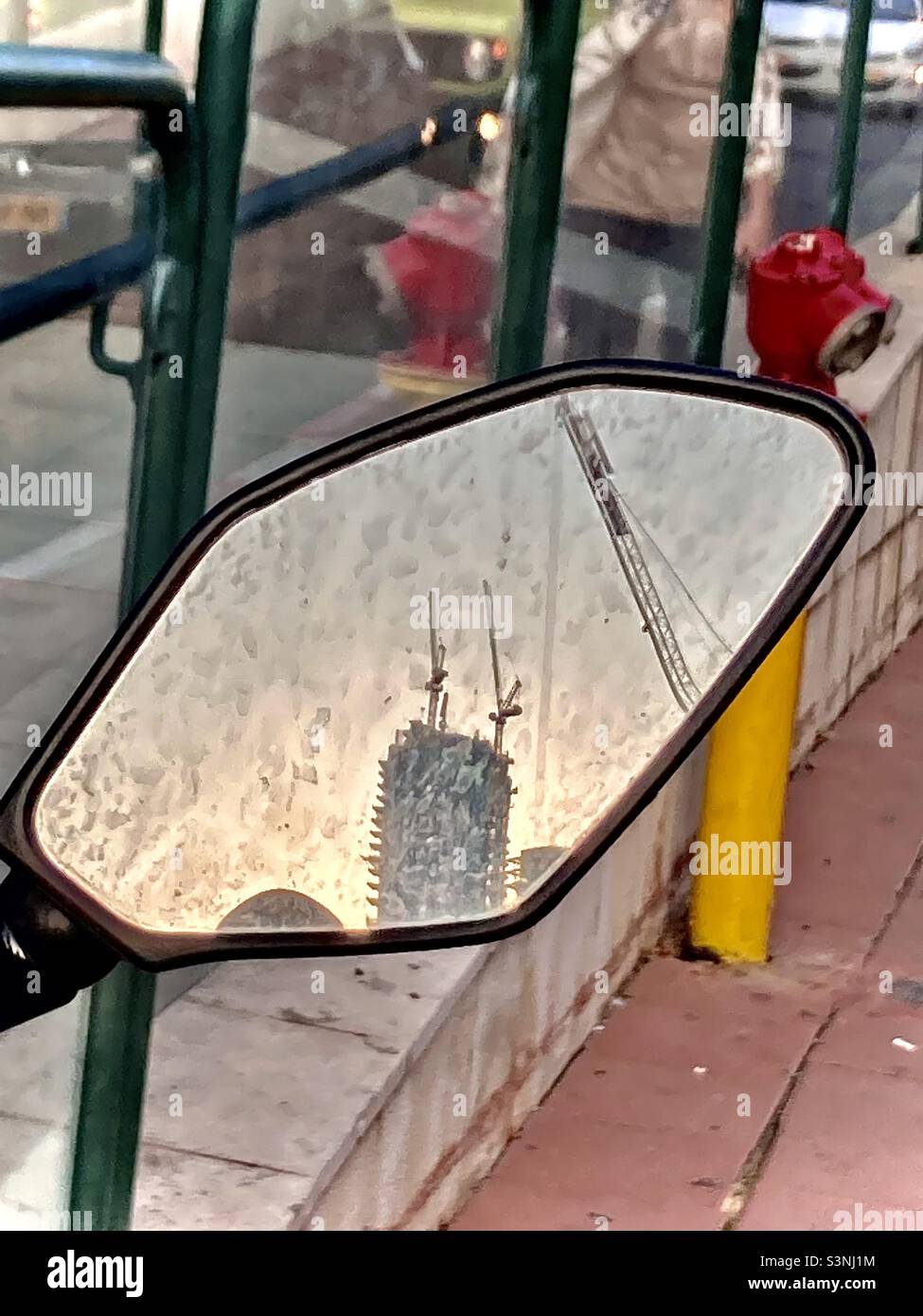 Costruzione di edifici con gru riflesse nello specchio retrovisore della motocicletta Foto Stock