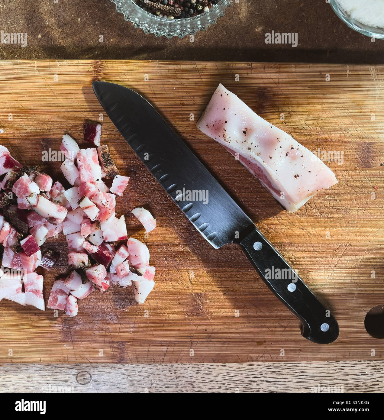 Pancetta tritata su un tagliere di legno con un coltello Foto Stock