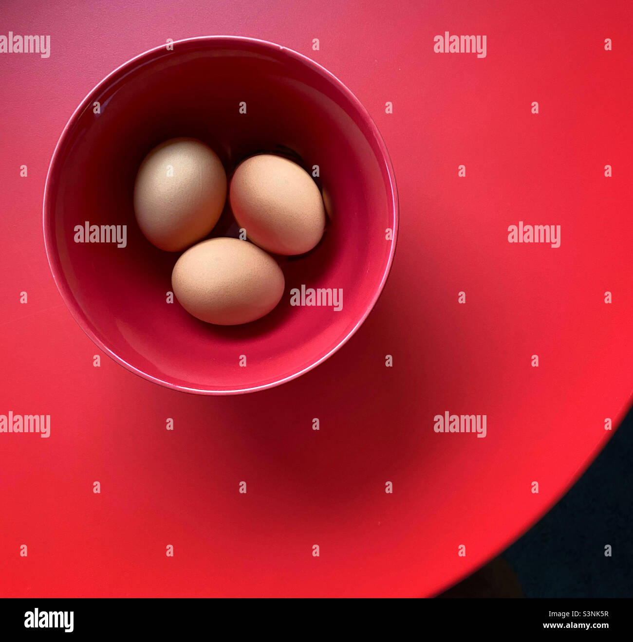 Rosolare le uova organiche in un recipiente rosso su un tavolo rosso - Immagine stock catturata con smartphone